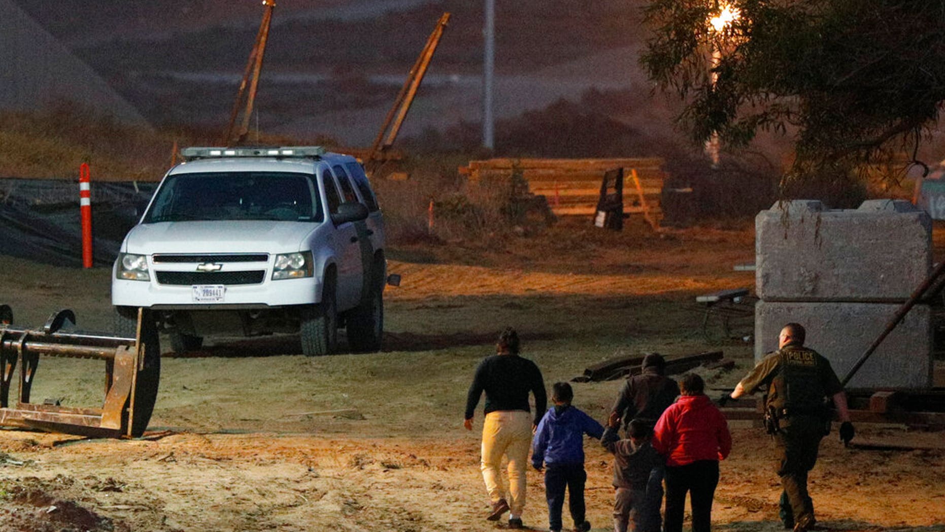 FILE - In this Dec. 3, 2018, file photo, migrants are escorted by a U.S. Border Patrol agent as they are detained after climbing over the border wall from Playas de Tijuana, Mexico, to San Ysidro, Calif. (AP Photo/Rebecca Blackwell, File)