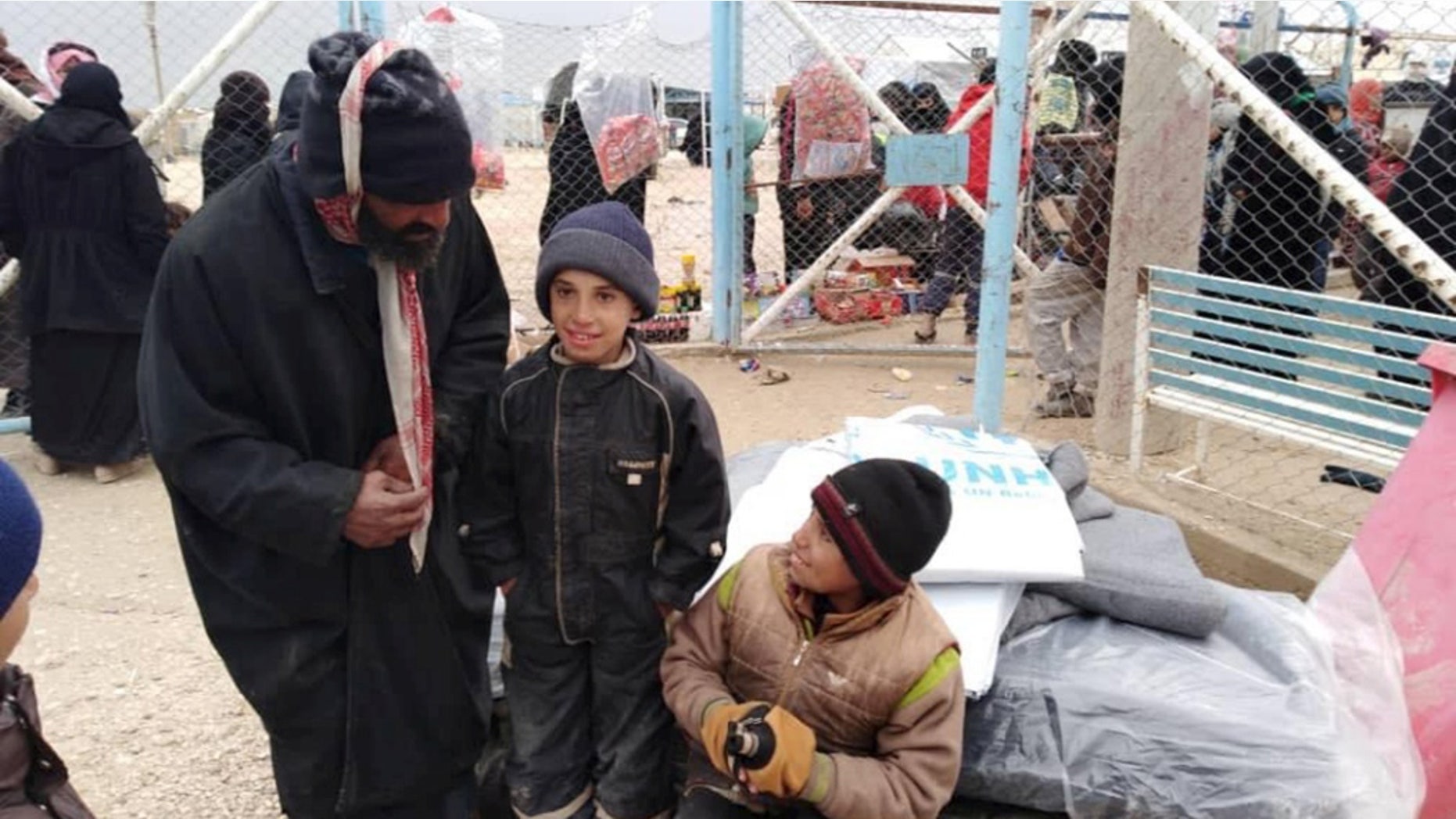 Newly displaced Syrian children and men wait to receive UNHCR tarpaulins and other aid at Al Hol camp in Hassakeh, Syria.