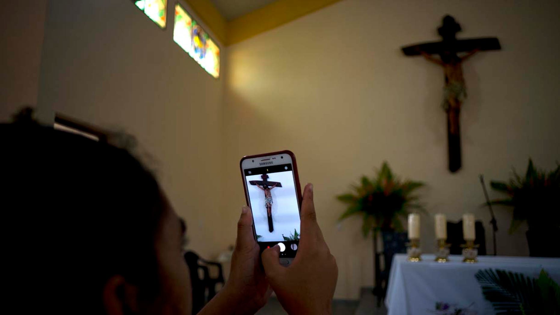A parishioner makes a photo of the crucifix above the altar at the newly consecrated Sagrado Corazon de Jesus, or Sacred Heart, Catholic church, in Sandino, Cuba, Saturday, Jan. 26, 2019. (AP Photo/Ramon Espinosa)