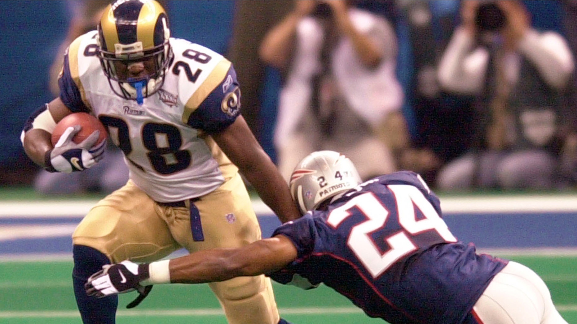 File-This Feb. 3, 2002, file photo shows St. Louis Rams running back Marshall Faulk (28) fending of New England Patriots cornerback Ty Law (24) during first-quarter play of Super Bowl XXXVI in New Orleans.