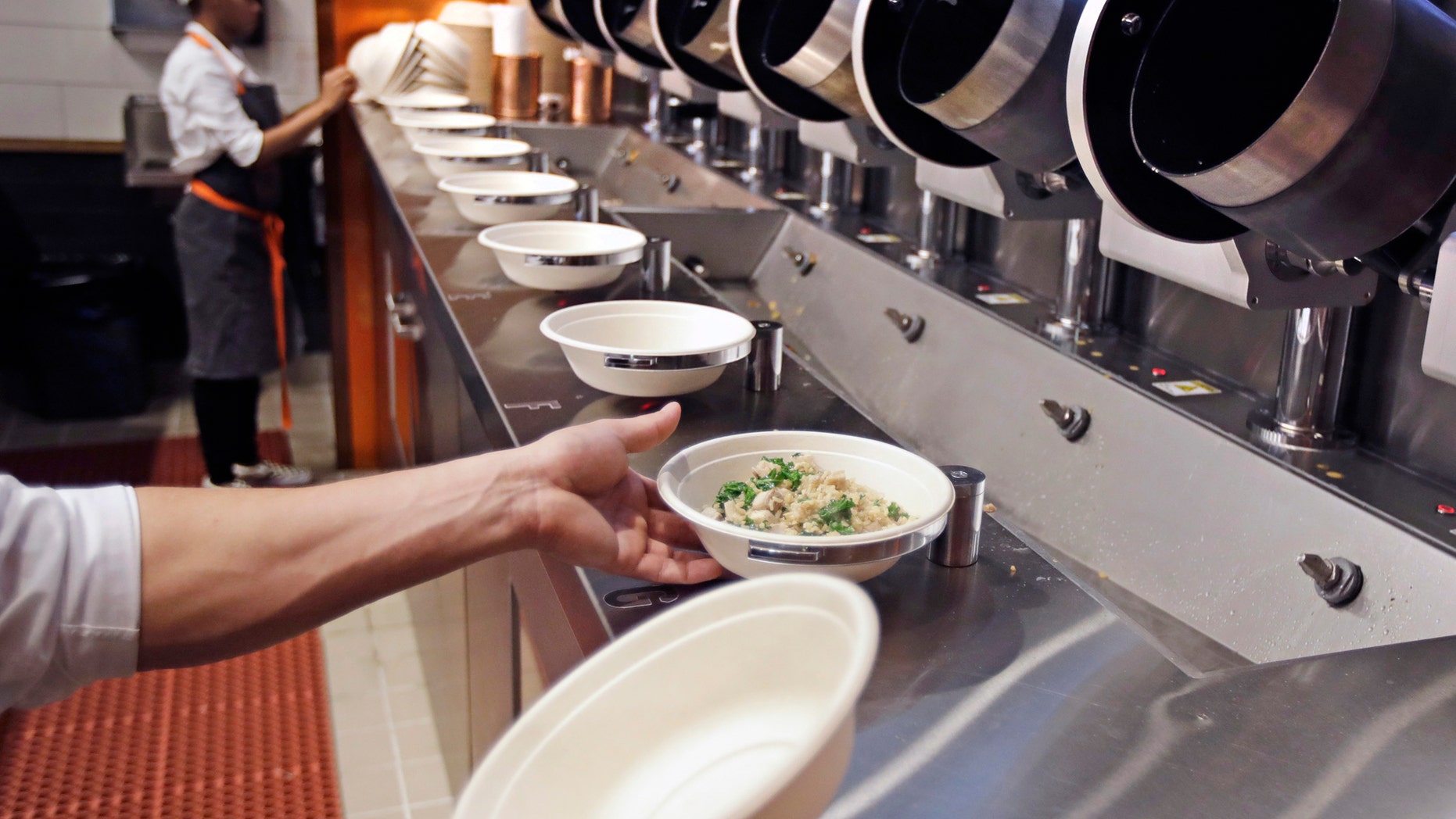 FILE- In this May 3, 2018, file photo a worker lifts a lunch bowl off the production line at Spyce, a restaurant which uses a robotic cooking process, in Boston. Robots aren’t replacing everyone, but a quarter of U.S. jobs will be severely disrupted as artificial intelligence accelerates the automation of today’s work, according to a new Brookings Institution report published Thursday, Jan. 24, 2019. (AP Photo/Charles Krupa, File)