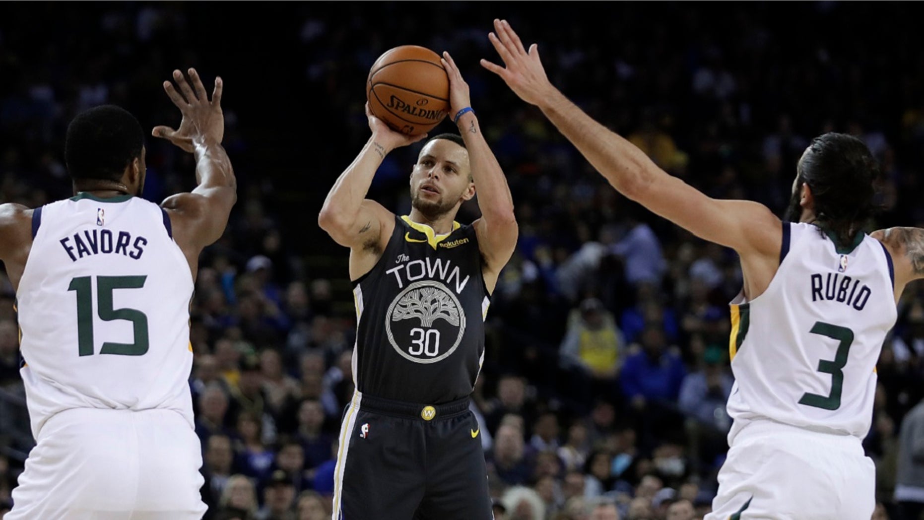 Golden State Warriors' Stephen Curry, center, shoots between Utah Jazz's Derrick Favors (15) and Ricky Rubio (3) during the second half of an NBA basketball game Tuesday, Feb. 12, 2019, in Oakland, Calif. (Associated Press)
