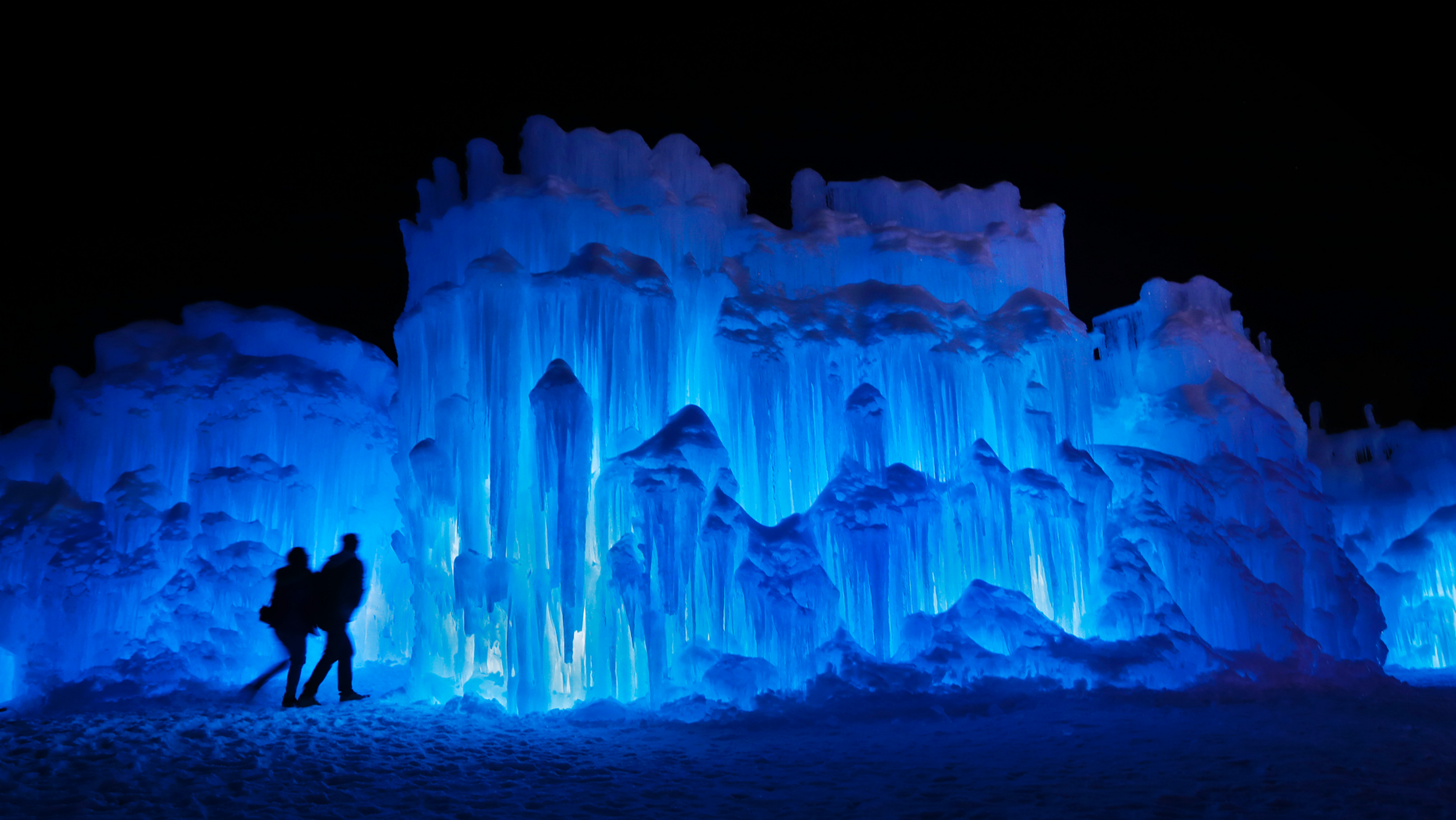 In this Saturday, Jan. 26, 2019 photo, a couple heads towards an entrance to a cavern at Ice Castles in North Woodstock, N.H. A team starts building massive walls in December to create a spectacular winter experience. (AP Photo/Robert F. Bukaty)