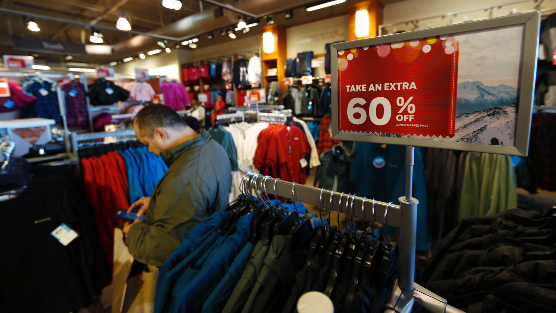 FILE- In this Dec. 24, 2018, photo a last-minute shopper scans his mobile device next to a sign marking discounts on coats at Columbia store as shoppers finish up their Christmas gift lists at the Outlet Malls in Castle Rock in Castle Rock, Colo. The On Thursday, Feb. 14, 2019, the Commerce Department releases U.S. retail sales data for December. (AP Photo/David Zalubowski, File)