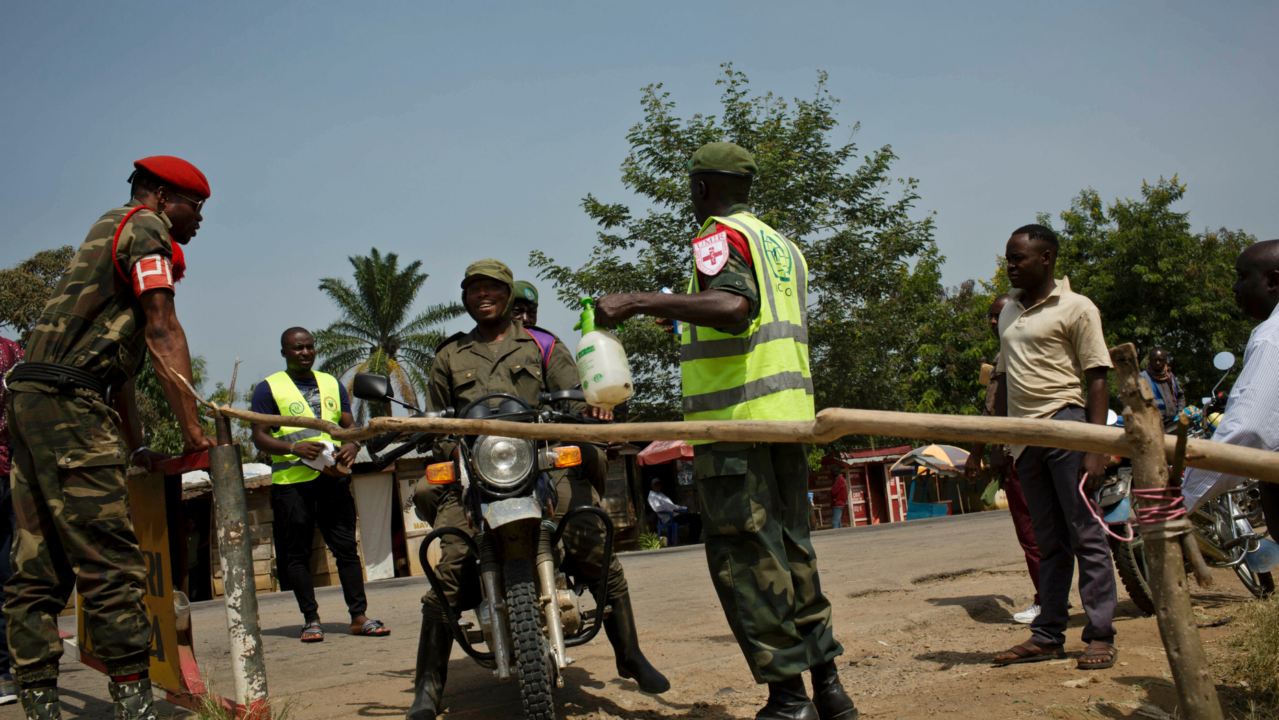 Two Congolese government soldiers have their feet and motorcycle tires sprayed with bleach as part of an Ebola containment program on the road between Beni and Oicha, in Congo Friday, Feb. 1, 2019.