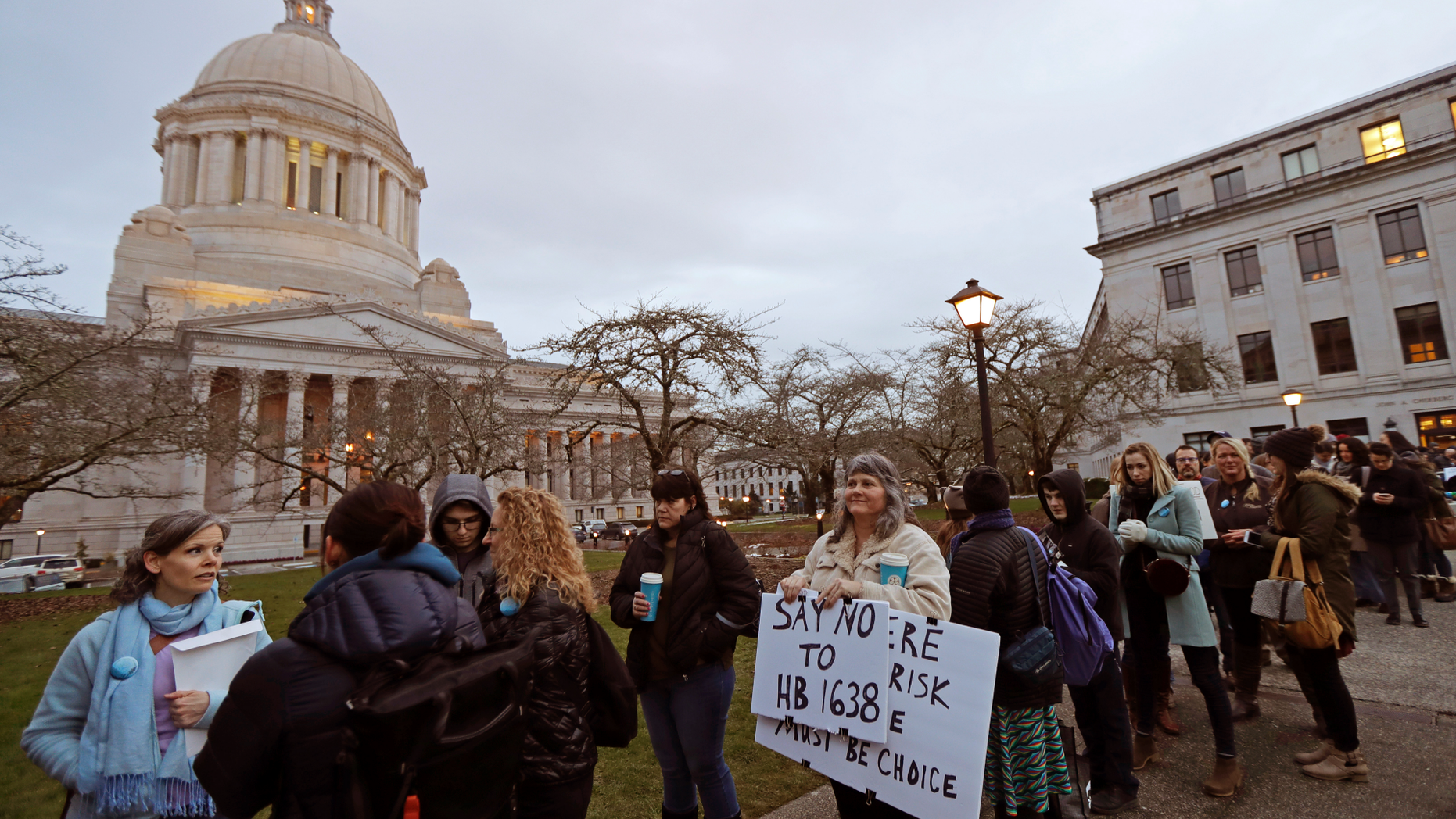 Kebby Johnson, center, of Spokane, Wash., holds a sign that reads "Say No to HB 1638," as she waits in line, Friday, Feb. 8, 2019, to attend a public hearing before the House Health Care & Wellness Committee at the Capitol in Olympia, Wash. Amid a measles outbreak that has sickened people in Washington state and Oregon, lawmakers heard public testimony Friday on a bill that would remove parents' ability to claim a philosophical exemption to opt their school-age children out of the combined measles, mumps and rubella vaccine. (AP Photo/Ted S. Warren)