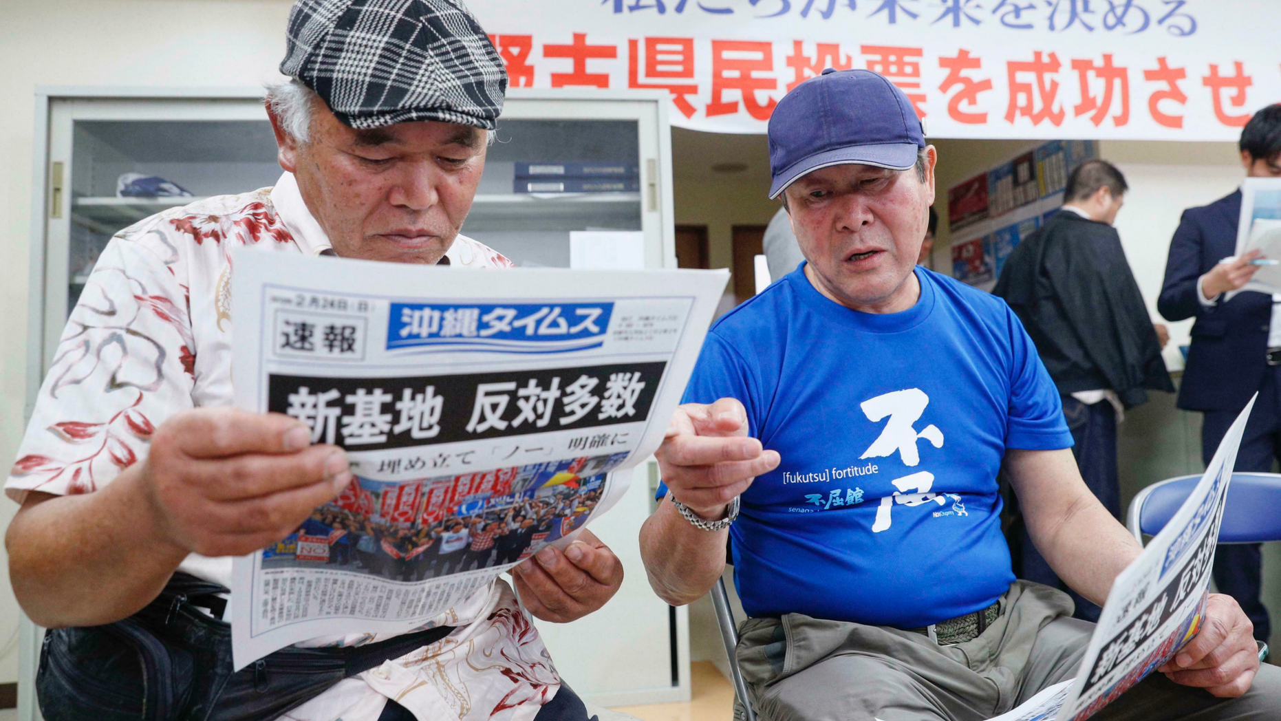 People take a look at a copy of a local newspaper reporting a referendum in Naha, Okinawa, Japan, Sunday, Feb. 24, 2019. The people of Okinawa voted Sunday on a plan for a U.S. military base relocation in a referendum that will send a message on how they feel about housing American troops in Japan, who many see as a burden on the group of tiny southwestern islands. The headline reads "New Base, Opposition majority."(Kyodo News via AP)