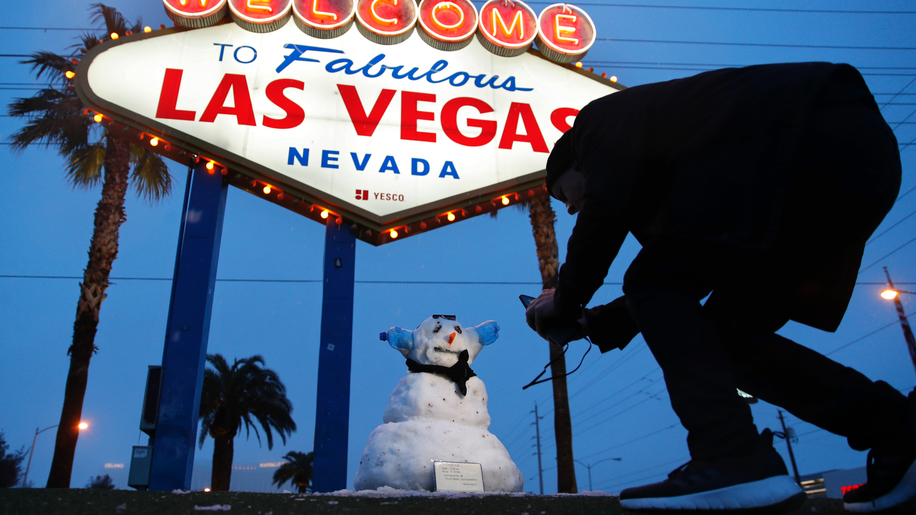 A man, who declined to give his name, takes a picture of a small snowman at the "Welcome to Fabulous Las Vegas" sign along the Las Vegas Strip, Thursday, Feb. 21, 2019, in Las Vegas. Las Vegas is getting a rare taste of real winter weather, with significant snowfall across the metro area in the first event of its kind since record keeping started back in 1937. (AP Photo/John Locher)