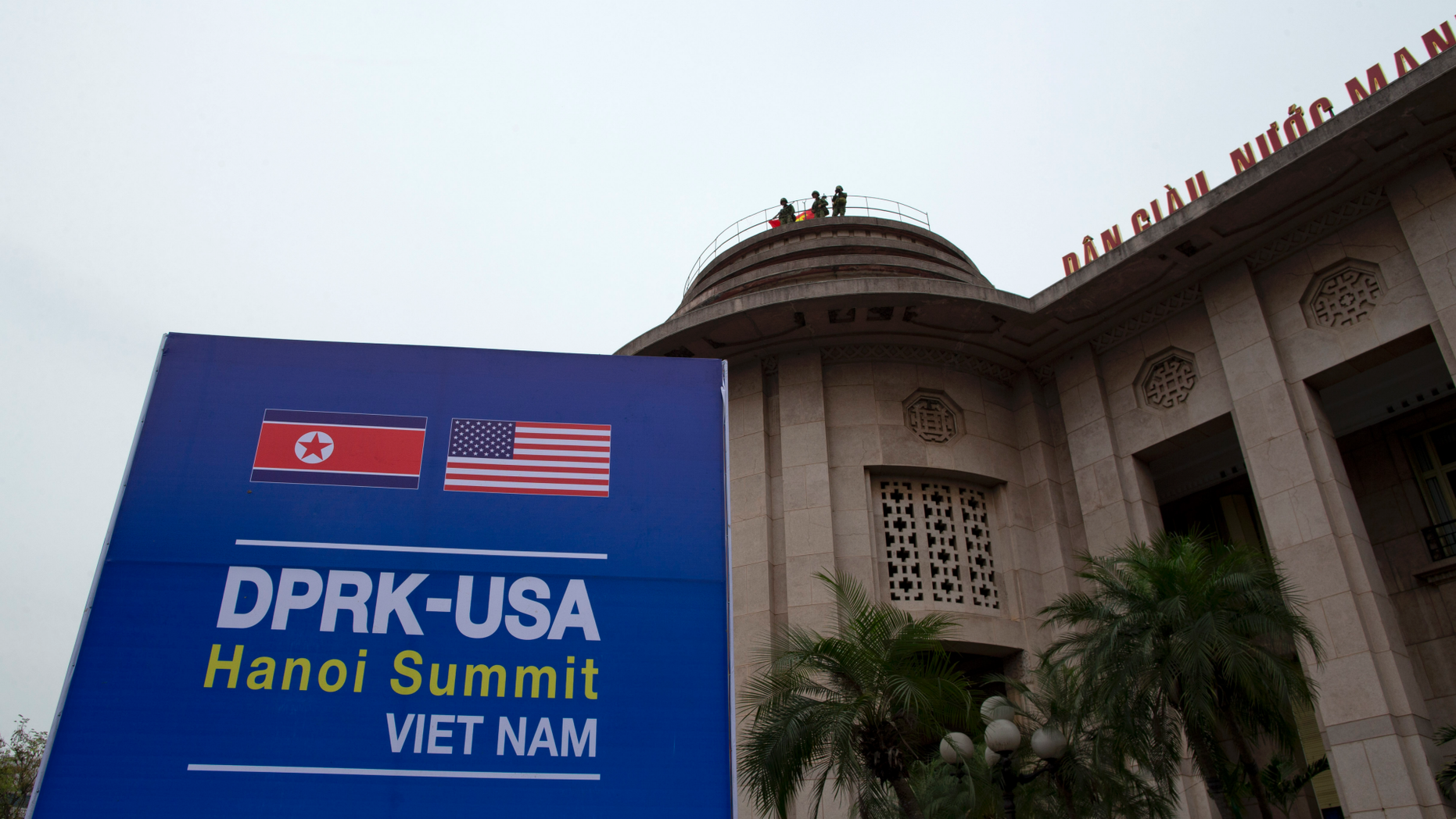 Vietnamese soldiers watch from a top of a building neighboring Government Guesthouse and the Metropole hotel next to a poster featuring upcoming summit between the U.S. and North Korea in Hanoi, Vietnam, Sunday, Feb. 24, 2019. The second summit between U.S President Donald Trump and North Korean leader Kim Jong Un will take place in Hanoi on Feb. 27 and 28. (AP Photo/Gemunu Amarasinghe)