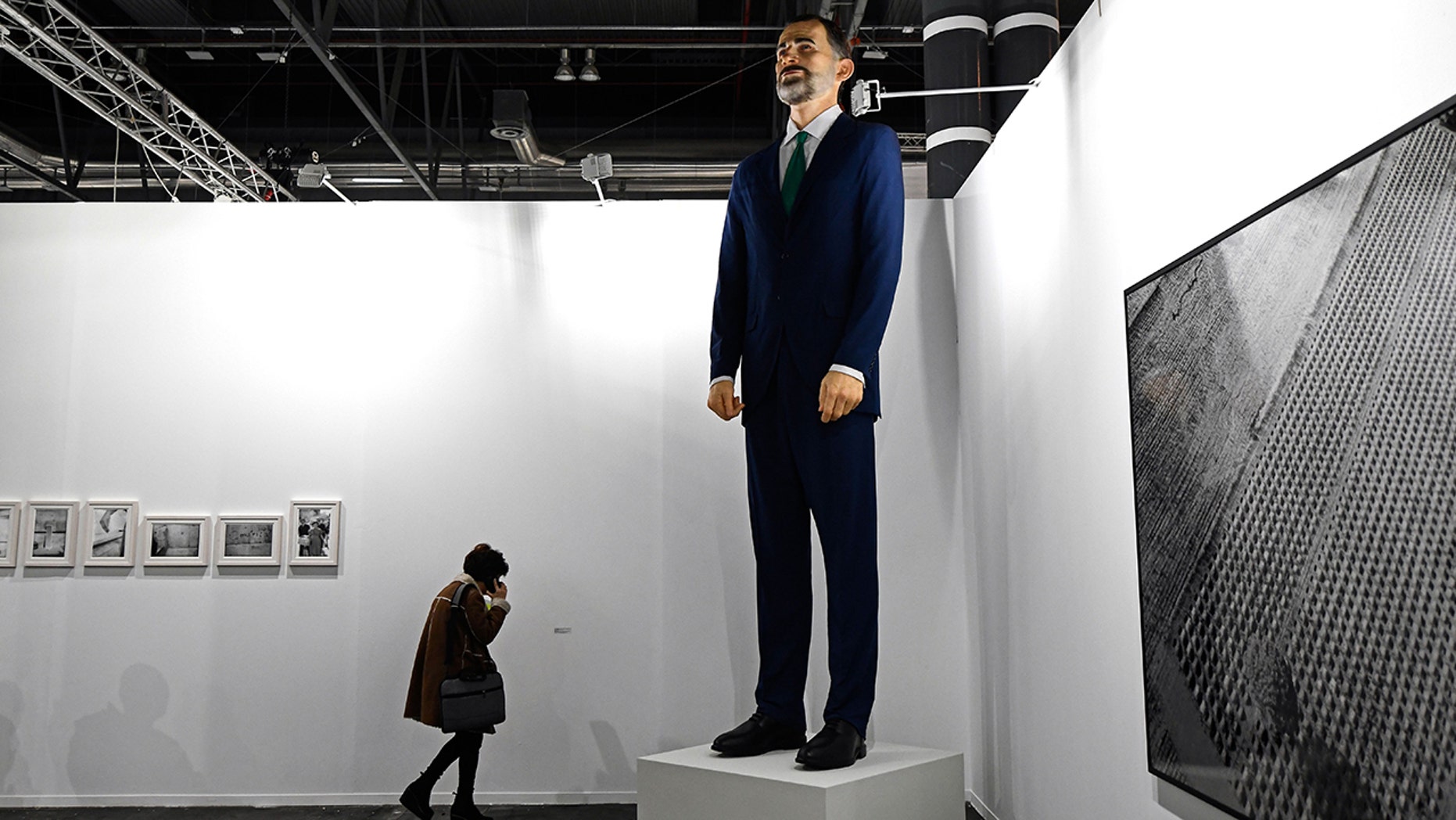 A woman talks on her mobile phone next to "Ninot", a giant sculpture depicting Spain's King Felipe VI by artists Santiago Sierra and Eugenio Merino, during preparations for the International Contemporary Art Fair (ARCO) in Madrid on February 26, 2019 on the eve of its inauguration. 