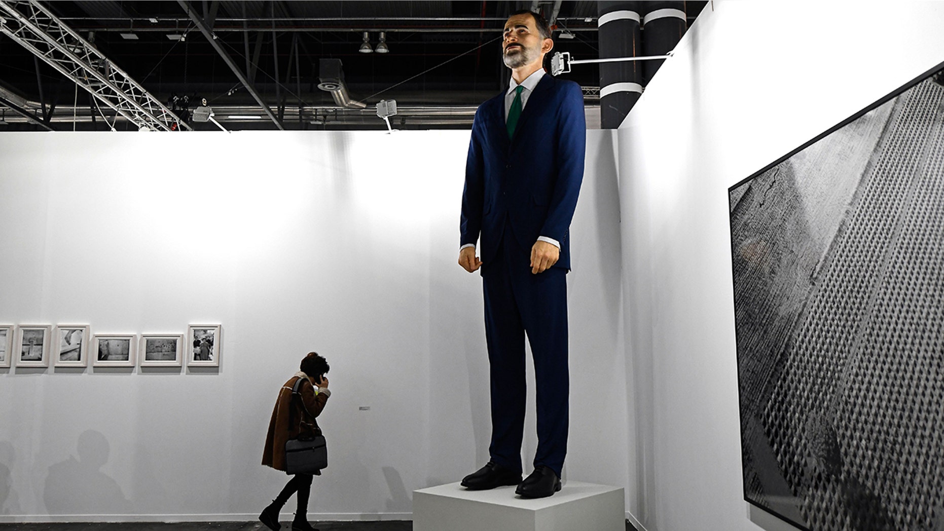 A woman talks on her mobile phone next to "Ninot", a giant sculpture depicting Spain's King Felipe VI by artists Santiago Sierra and Eugenio Merino, during preparations for the International Contemporary Art Fair (ARCO) in Madrid on February 26, 2019 on the eve of its inauguration.