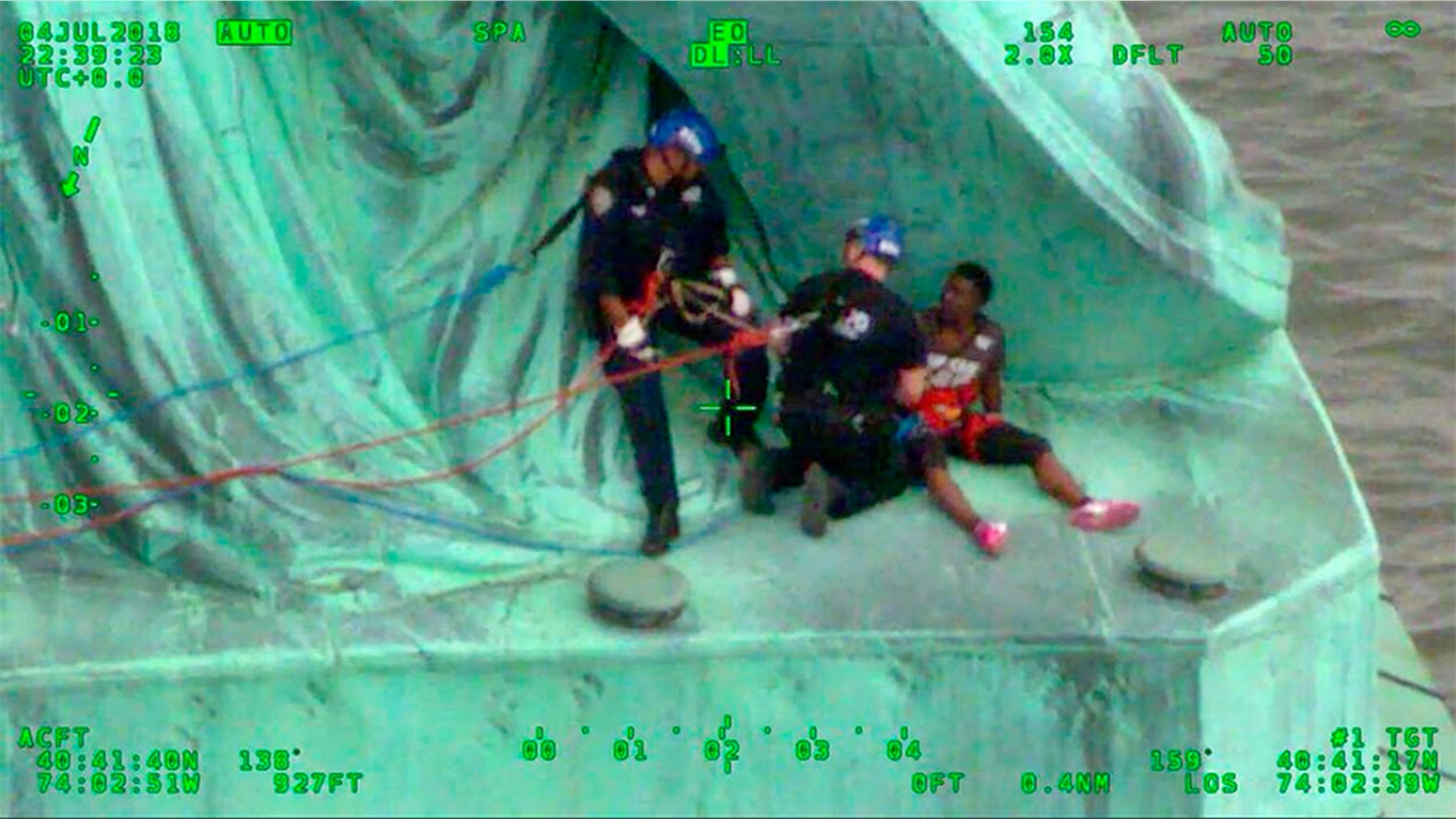 In this July 4, 2018, frame from video provided by the New York City Police Department, members of the NYPD Emergency Service Unit work to safely remove Therese Okoumou, a protester who climbed onto the Statue of Liberty and was charged with misdemeanor trespassing and disorderly conduct. (NYPD via AP)