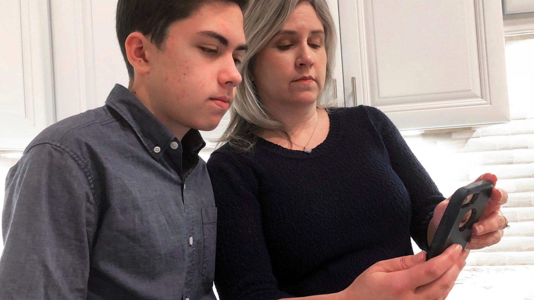 FILE- On January 31, 2019, Grant Thompson and his mother, Michele, are watching an iPhone in the family kitchen in Tucson, Arizona, on Thursday, January 31, 2019. (AP Photo / Brian Skoloff, File)