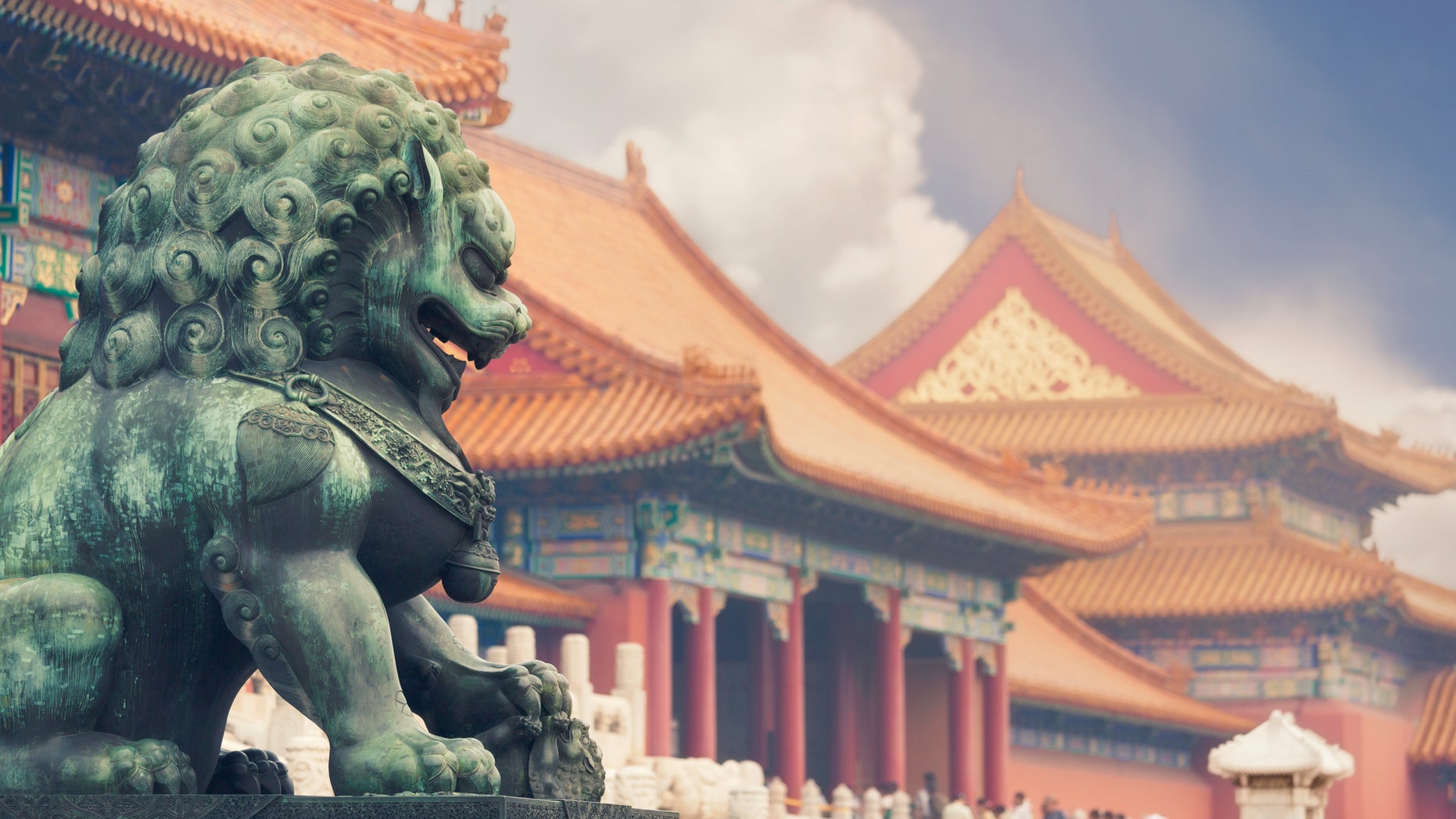 An old imperial lion sculpture in seen in front of historical Forbidden City buildings.