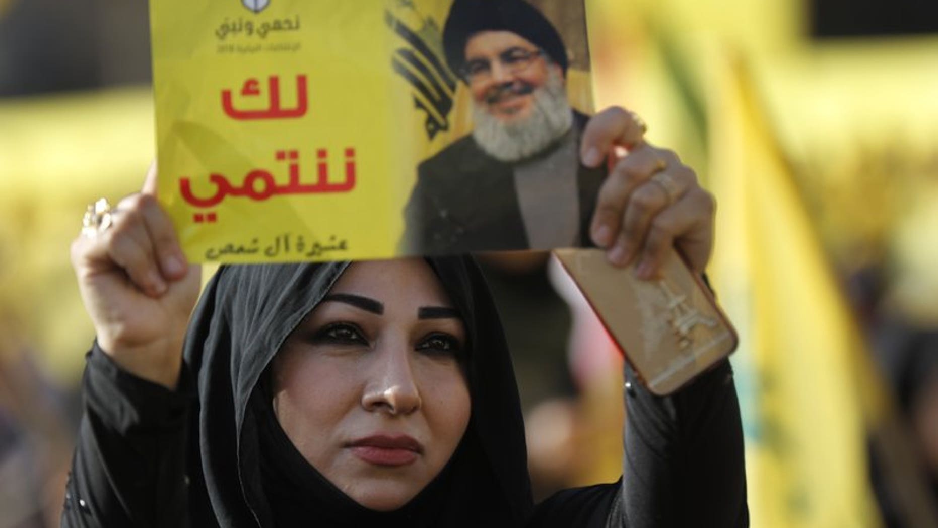 In this April 13, 2018, file photo, a supporter of Hezbollah leader Sayyed Hassan Nasrallah holds up his portrait with Arabic words that read: "We belong with you," during an election campaign speech in a southern suburb of Beirut, Lebanon.