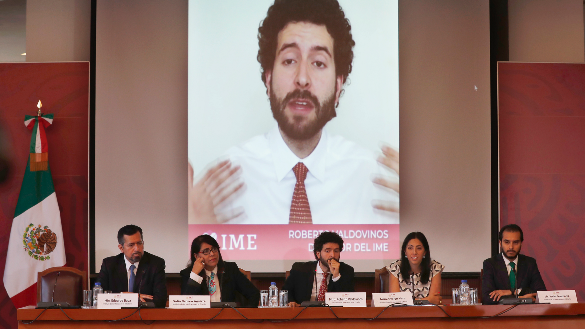 Roberto Valdovinos, head of the Institute for Mexicans Abroad, is shown speaking in a video behind as he gives a news conference, sitting center, in Mexico City, Thursday, March 14, 2019. The Mexican government is launching open-ended public consultation forums in the U.S. to give Mexicans living there a chance to opine on Mexico's national development plan. (AP Photo/Marco Ugarte)