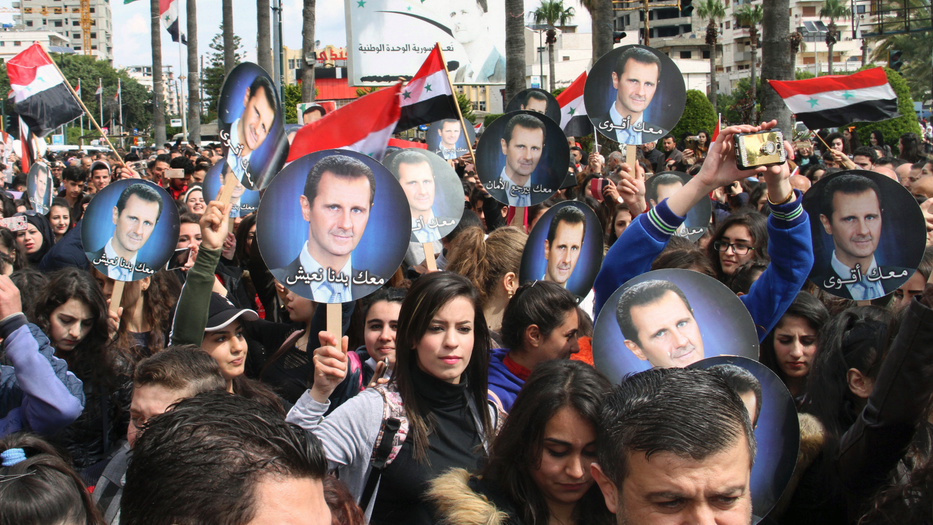 In this photo released by the Syrian official news agency SANA, people hold Syrian flags and portraits of President Bashar Assad during a protest against U.S. President Donald Trump's move to recognize Israeli sovereignty over the Israeli occupied Golan Heights, in the costal port city of Tartus, Syria, Wednesday, March. 27, 2019. (SANA via AP)