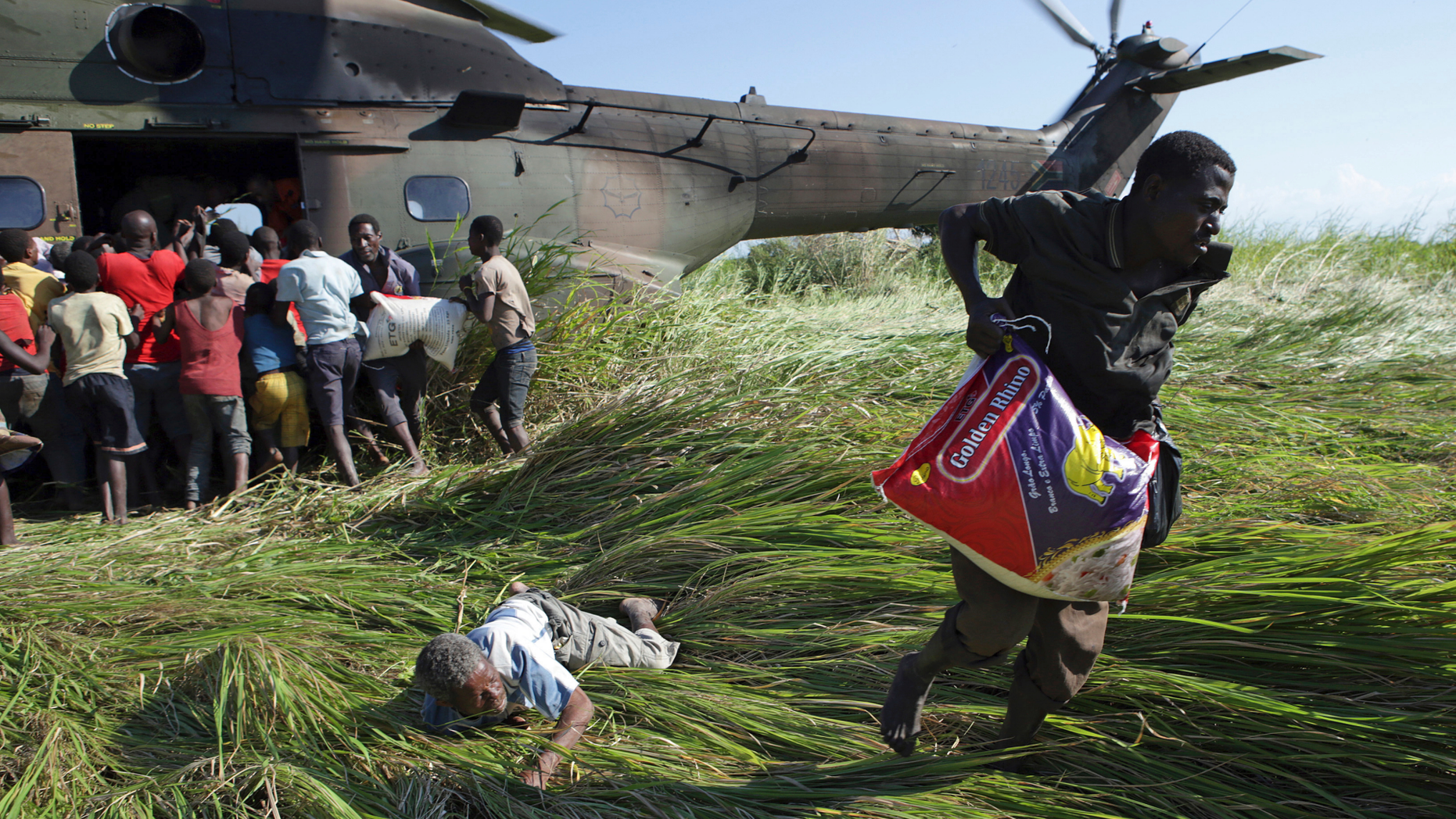 In this Tuesday, March 26, 2019, photo, an elderly man lies on the ground after his bag of food was snatched from him in a scramble for bags of rice delivered by the South African Airforce helicopter at Nyamatande Village, Mozambique, following the devastating Tropical Cyclone Idai. A second week has begun with efforts to find and help some tens of thousands of people in devastated parts of southern Africa, with some hundreds dead and an unknown number of people still missing. (AP Photo/Phill Magakoe)