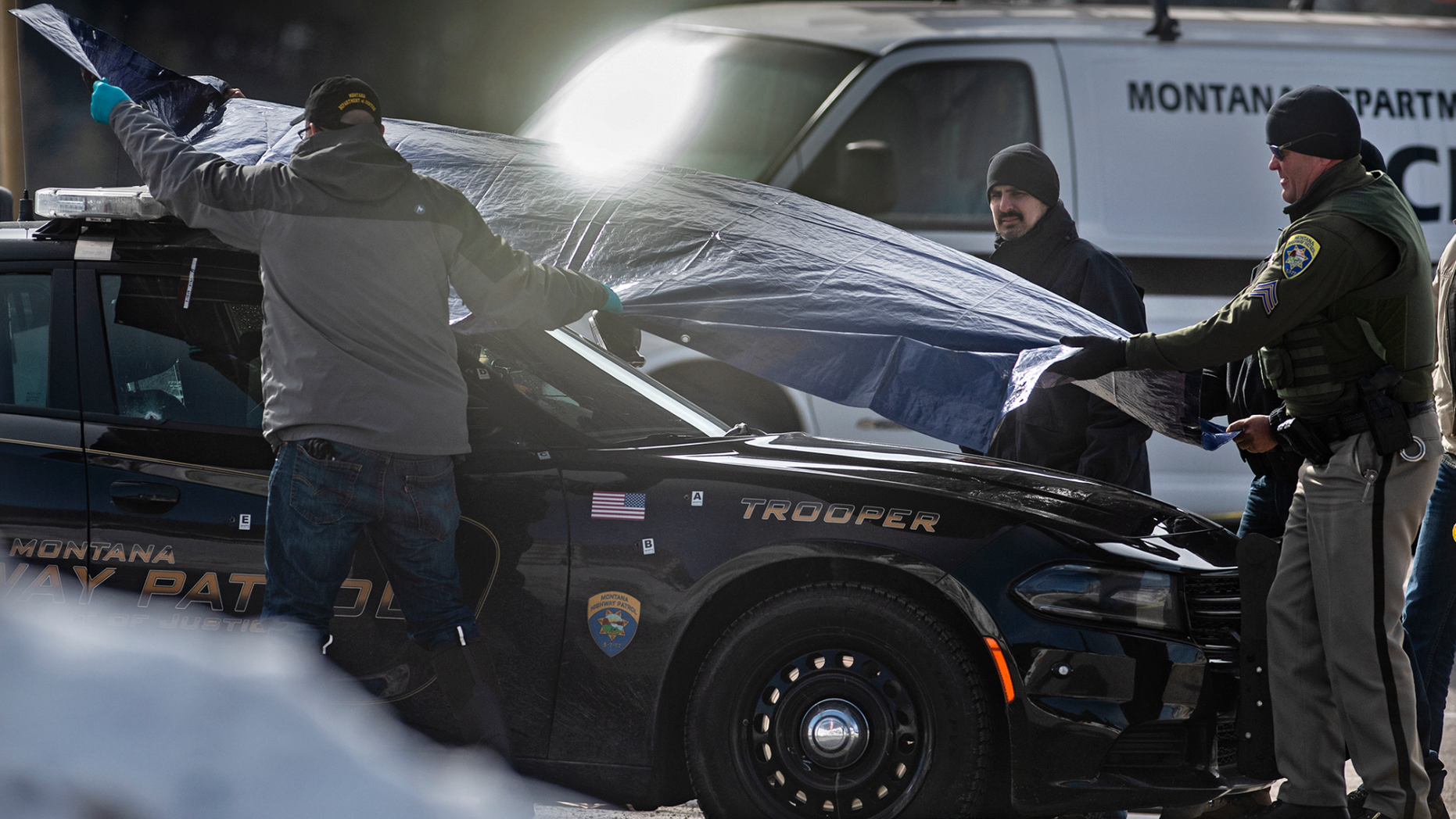 Law enforcement cover Montana State Trooper Wade Palmer's car at the scene of the shooting near the Evaro Bar on Friday, March 15, 2019, in Missoula, Mont. Palmer, who was investigating an earlier shooting, was himself shot and critically injured early Friday after finding the suspect's vehicle, leading authorities to launch an overnight manhunt that ended in the arrest of a 29-year-old man, officials said. (Tommy Martino/The Missoulian via AP)