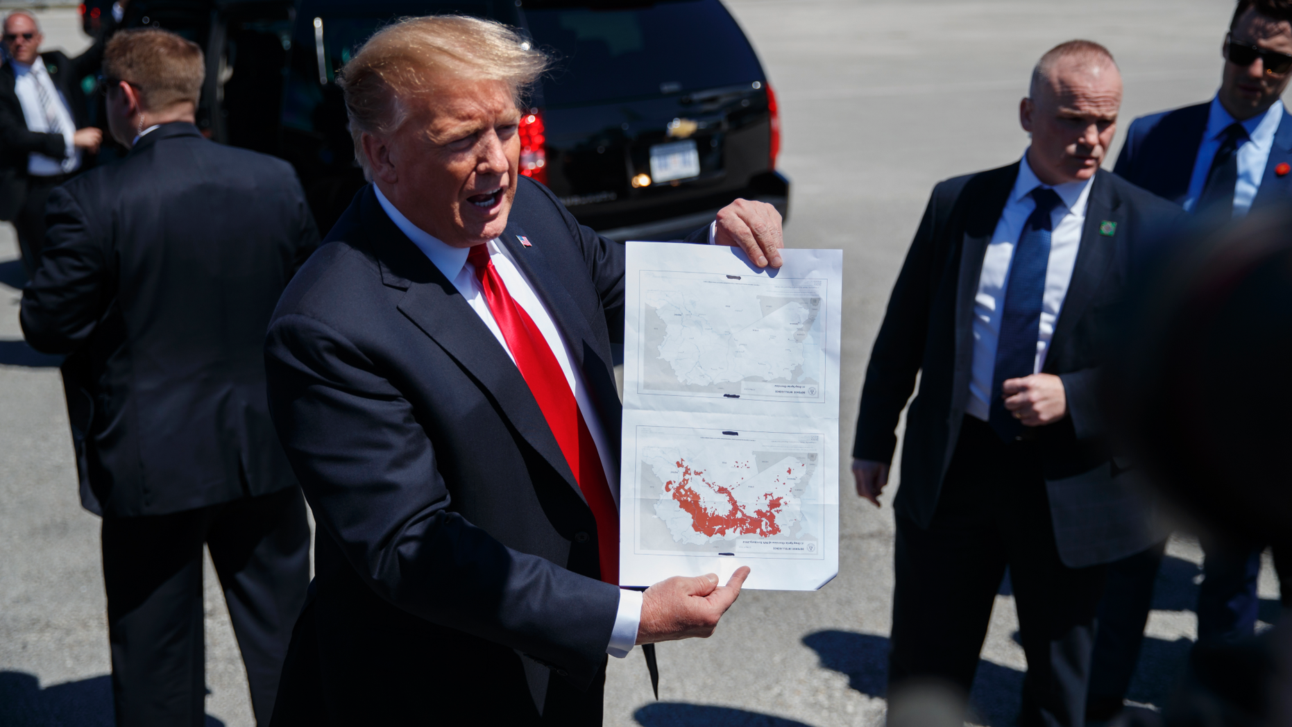 President Donald Trump holds a a copy of two maps of Syria as he arrives on Air Force One, Friday, March 22, 2019, at Palm Beach International Airport, in West Palm Beach, Fla. One map is awash in red shows IS controlled territory in Syria in November 2016. The other, without red, indicates that IS as of today no longer controls territory in Syria. (AP Photo/Carolyn Kaster)
