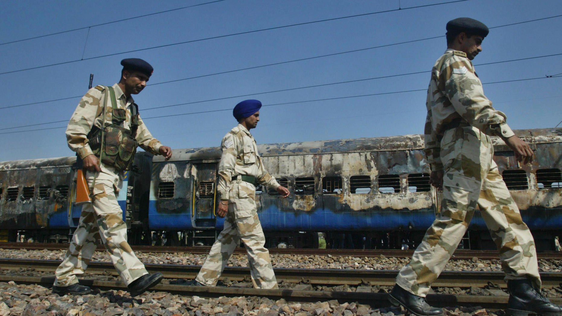 FILE - In this Feb. 19, 2007, file photo, Indian security personnel walk past the charred coaches of Samjauta Express train, or Friendship Express, which caught fire after a blast at Dewana, about 80 kilometers (50 miles) north of New Delhi, India. An Indian court has on Wednesday, March 20, 2019, acquitted four Hindu hardliners charged with triggering explosions in the train heading for India’s border with Pakistan 12 years ago, killing 68 people, mostly Pakistani nationals. (AP Photo/Mustafa Quraishi, File)