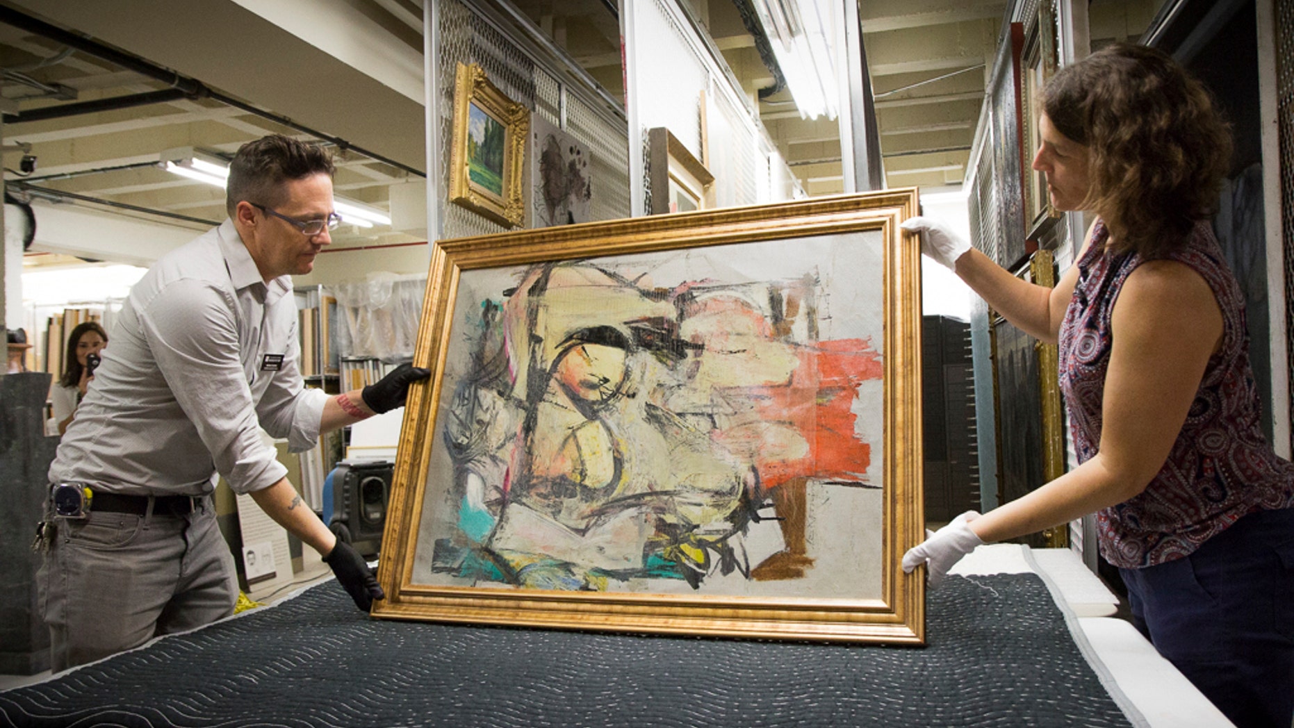 This August 2017 photo shows "Woman-Ochre," a painting by Willem de Kooning, being readied for examination by University of Arizona Museum of Art staff Nathan Saxton, left, and Kristen Schmidt in Tucson, Ariz. More than 30 years after it was stolen from the museum, the recovered painting will be on display back where it all began. (Robert Demers/University of Arizona Communications via AP)