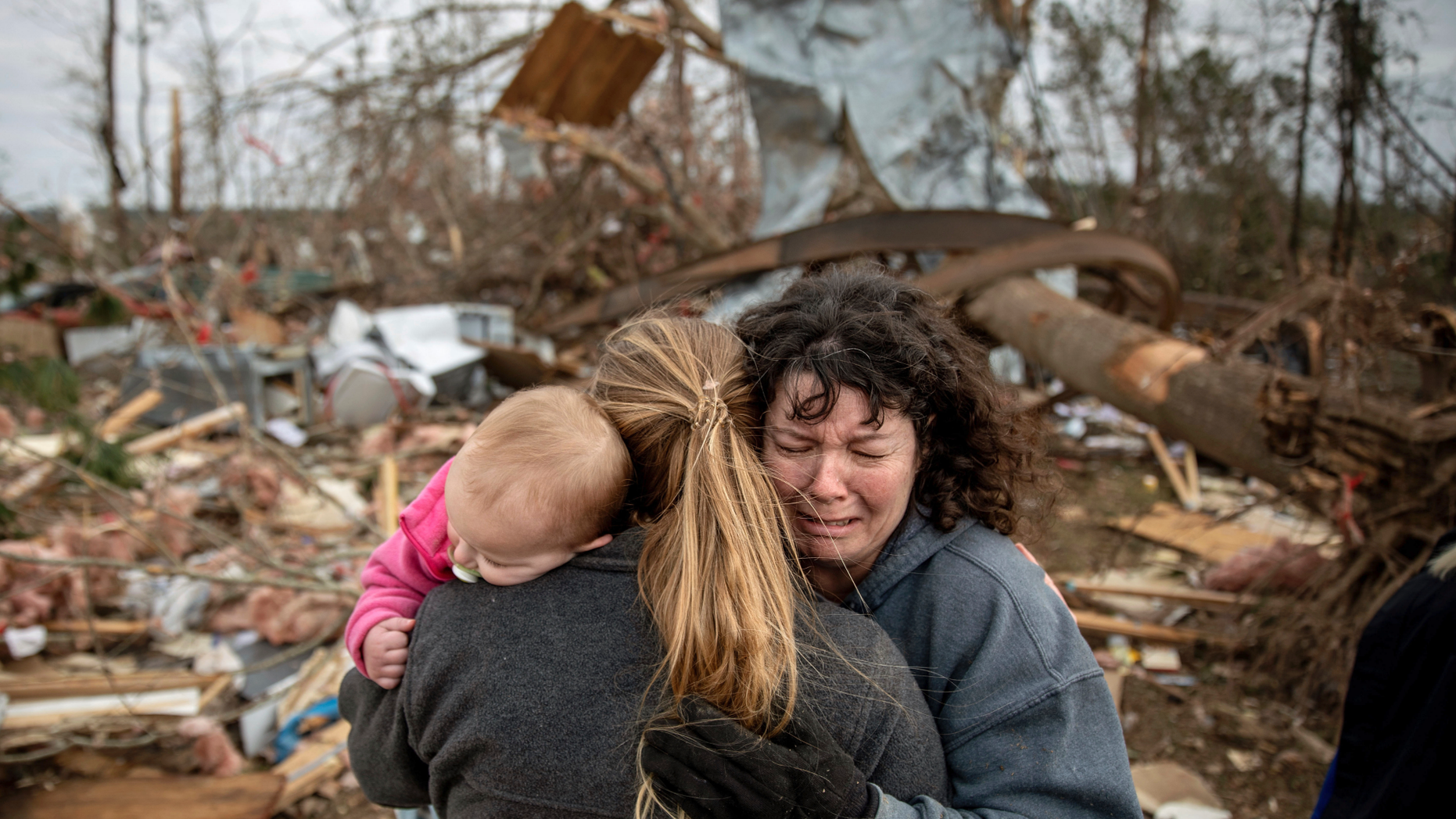 Carol Dean, right, cries while embraced by Megan Anderson and her 18-month-old daughter Madilyn, as Dean sifts through the debris of the home she shared with her husband, David Wayne Dean, who died when a tornado destroyed the house in Beauregard, Ala., Monday, March 4, 2019. "He was my wedding gift," said Dean of her husband whom she married three years ago. "He was one in a million. He'd send me flowers to work just to let me know he loved me. He'd send me some of the biggest strawberries in the world. I'm not going to be the same." (AP Photo/David Goldman)