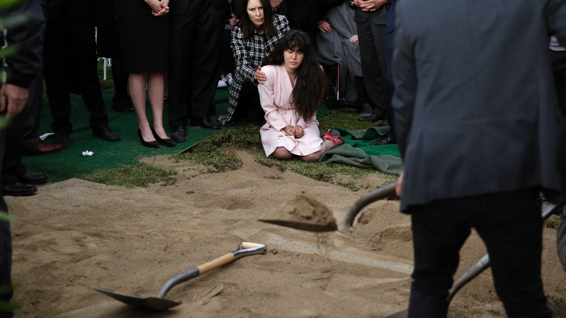 Hannah Kaye, center, the daughter of shooting victim Lori Kaye, sits on the ground with her aunt, Randi Grossman, as the last shovels of dirt cover her mother's grave during funeral services, Monday, April 29, 2019, in San Diego. Lori Kaye was killed when a man opened fire during Passover service on April 27 inside a synagogue near San Diego, as worshippers celebrated the last day of a major Jewish holiday. (AP Photo/Gregory Bull)