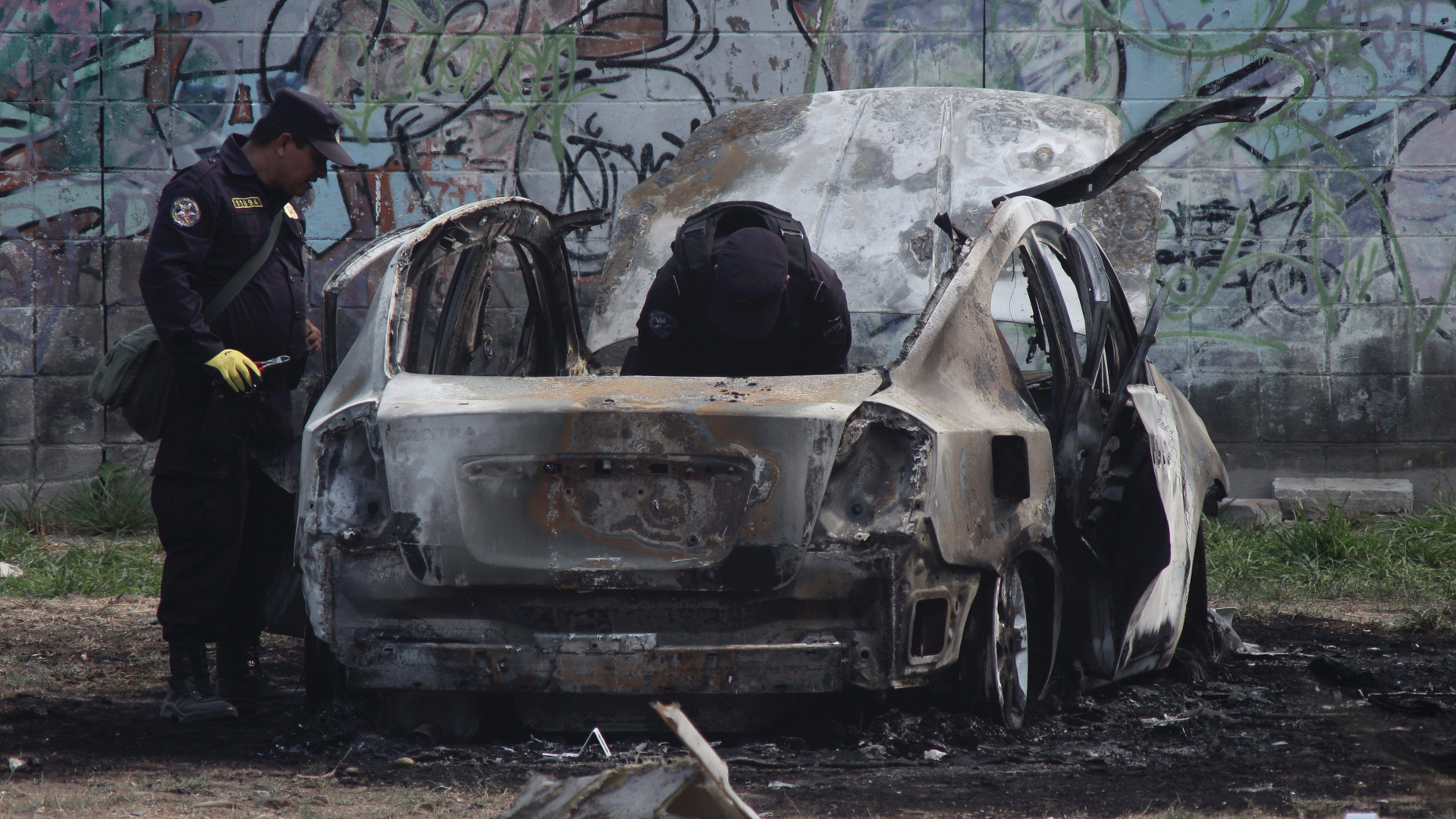 Police review the charred remains of a car that exploded as authorities responded to a report of a vehicle with a corpse inside, in the San Bartolo neighborhood of Soyapango, El Salvador, Monday, April 29, 2019. Two police officers were injured in the explosion. (AP Photo/Salvador Melendez)