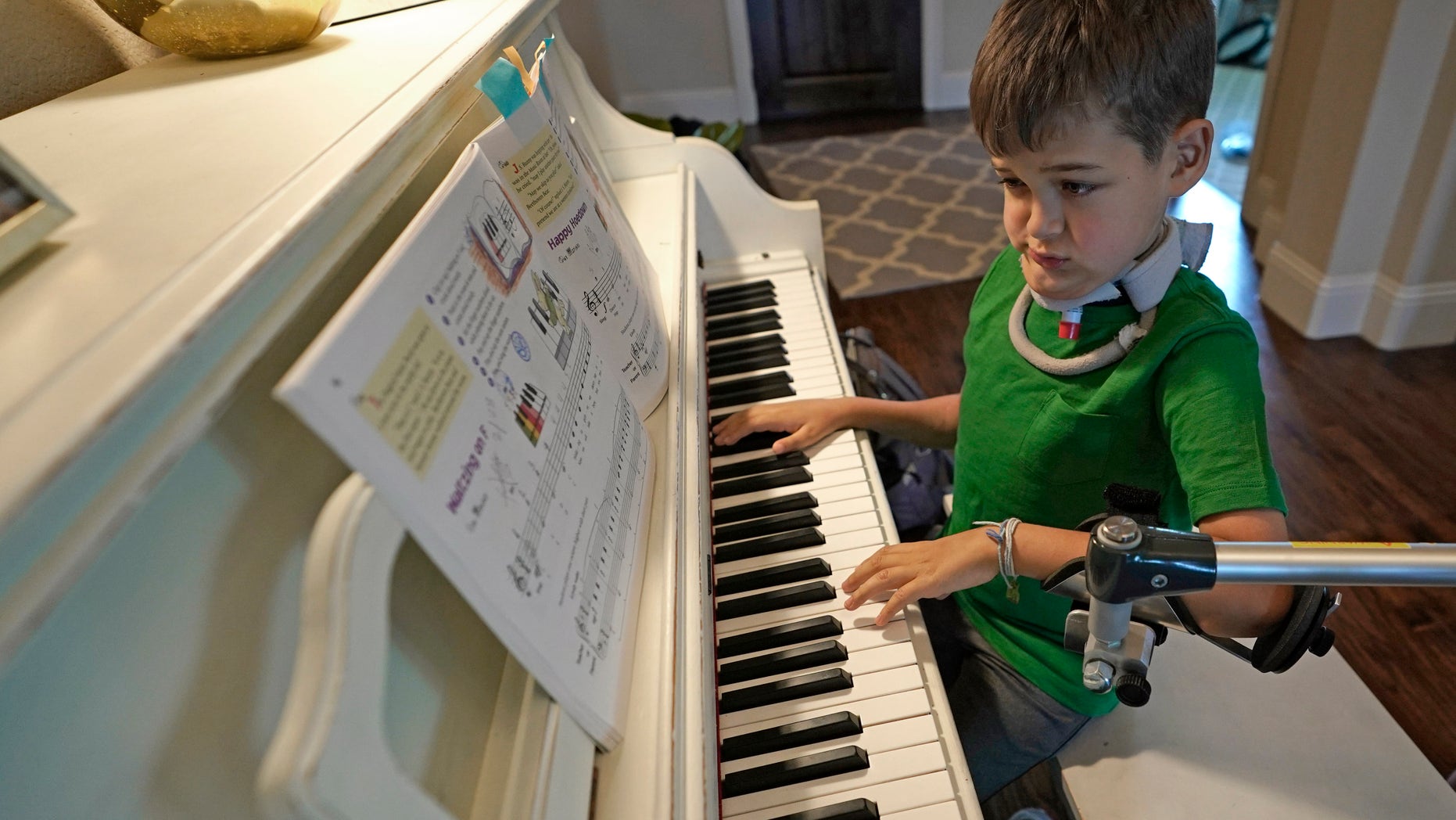 Braden Scott, who was diagnosed with ASM, uses a device that holds his left hand while practicing the piano in Tombole, Texas.