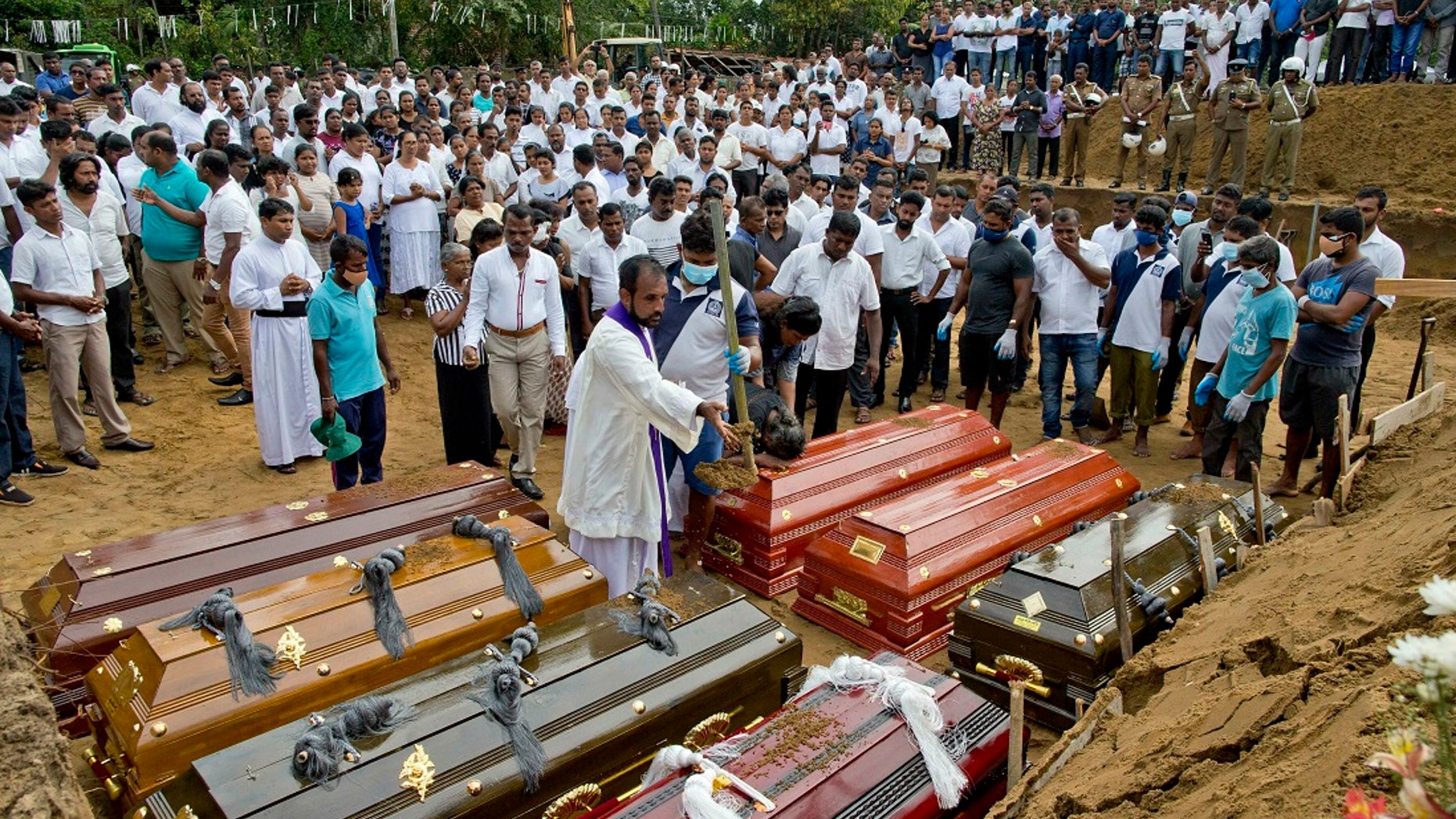 A priest conducts religious rituals during a mass burial for Easter Sunday bomb blast victims in Negombo, Sri Lanka, Wednesday, April 24, 2019. (AP Photo/Gemunu Amarasinghe)