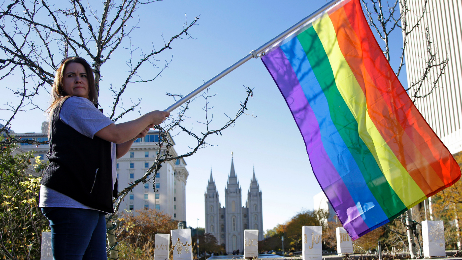 FILE - In this Nov. 14, 2015 file photo, Sandy Newcomb poses for a photograph with a rainbow flag as people gather for a mass resignation from The Church of Jesus Christ of Latter-day Saints in Salt Lake City. The Church of Jesus Christ of Latter-day Saints is repealing rules unveiled in 2015 that banned baptisms for children of gay parents and made gay marriage a sin worthy of expulsion. The surprise announcement Thursday, April 4, 2019, by the faith widely known as the Mormon church reverses rules that triggered widespread condemations from LGBTQ members and their allies. (AP Photo/Rick Bowmer, File)