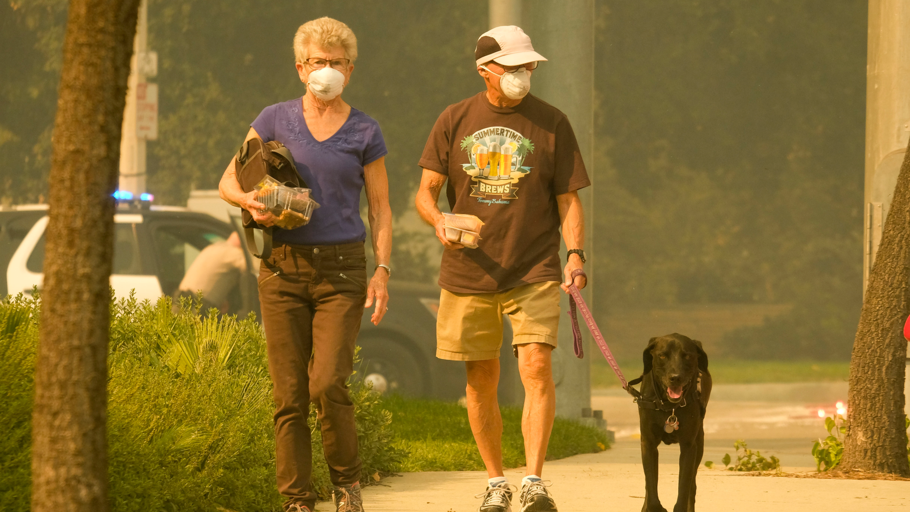 FILE - This Nov. 9, 2018, file photo people cover their faces walk their dog as smoke from a wildfire fills the air during the Woolsey Fire in Malibu, Calif. Wildfires are more frequent and fierce. When people can't evacuate, some are sheltering in place. It's a dicey strategy for all but the fortunate. (AP Photo/Ringo H.W. Chiu, File)