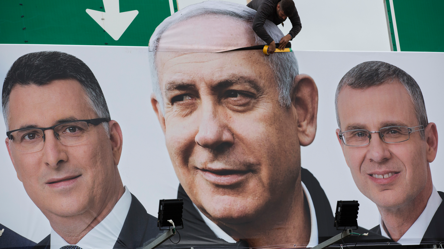 A man works on a Likud party election campaign billboard depicting Israeli Prime Minister Benjamin Netanyahu, center, and his party candidates, in Petah Tikva, Israel, Monday, April 1, 2019. (AP Photo/Oded Balilty)
