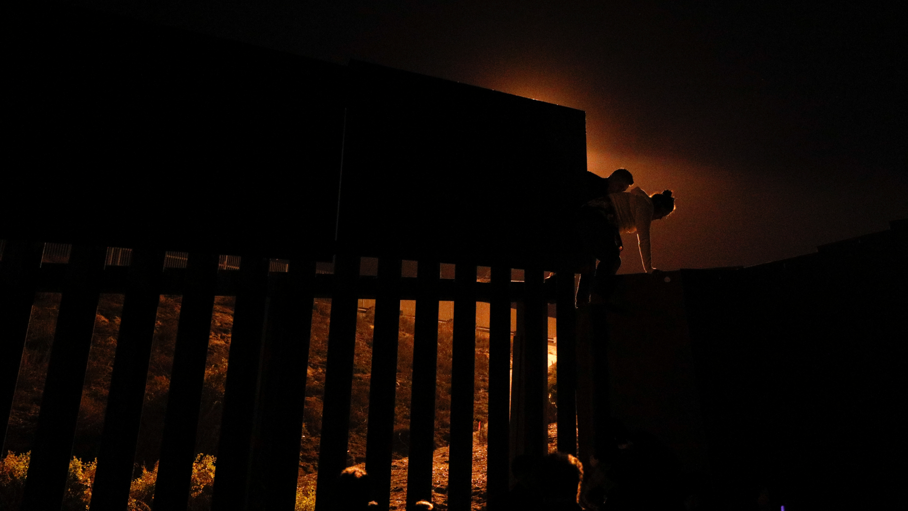 FILE - In this Dec. 2, 2018, file photo, Honduran migrants climb over a section of the U.S. border fence from Playas of Tijuana, Mexico, before handing themselves in to border control agents. A surge in family arrivals, largely from Guatemala and Honduras, has led Border Patrol agents to shift attention from preparing criminal cases to caring for children. (AP Photo/Rebecca Blackwell, File)