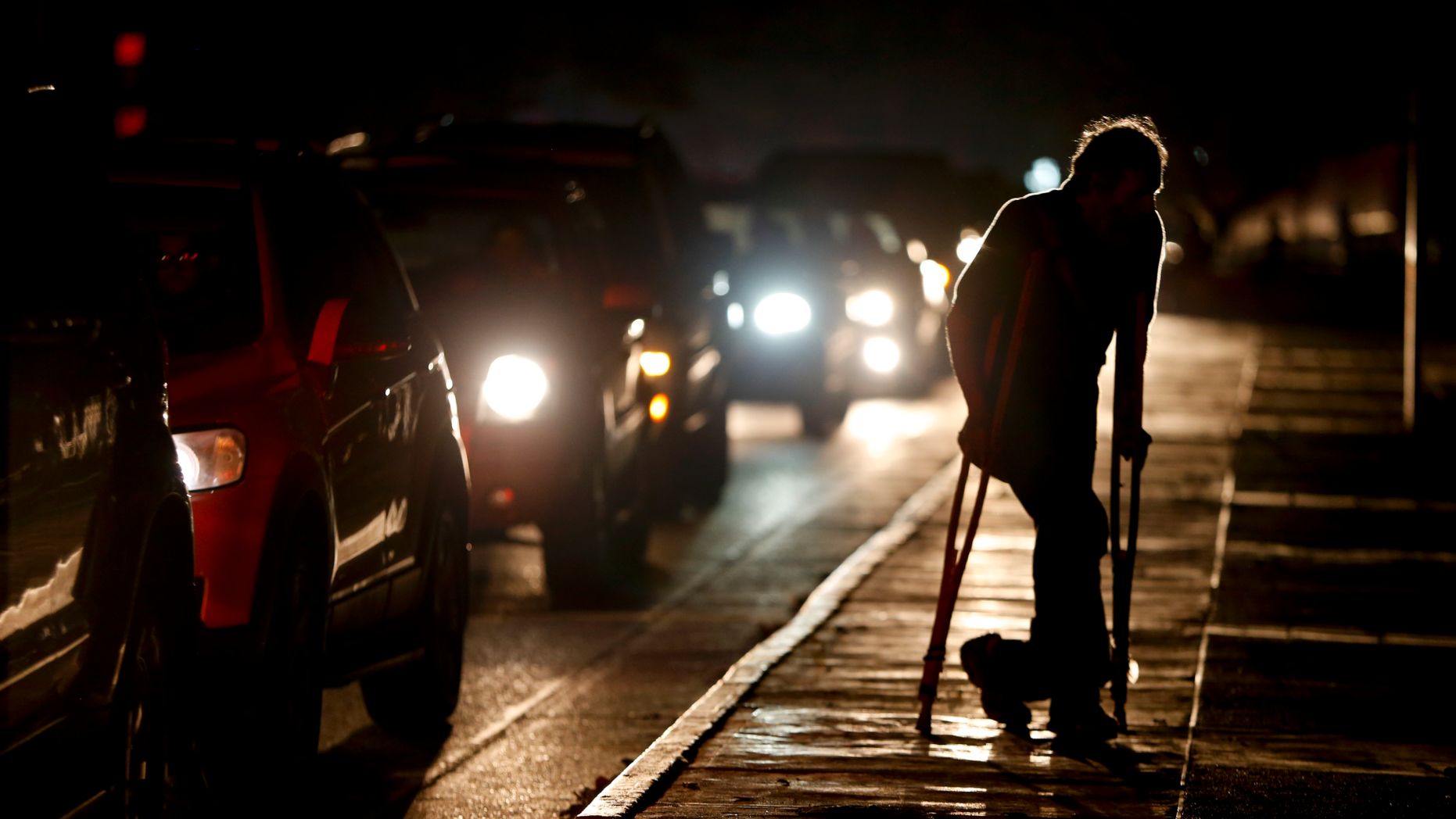 FILE - In this March 29, 2019 file photo, a man on crutches is illuminated by headlights of oncoming traffic, in Caracas, Venezuela. Venezuelans are struggling to understand the Sunday, March 31, 2019 announcement that the nation’s electricity is being rationed to combat daily blackouts. (AP Photo/Natacha Pisarenko, File)