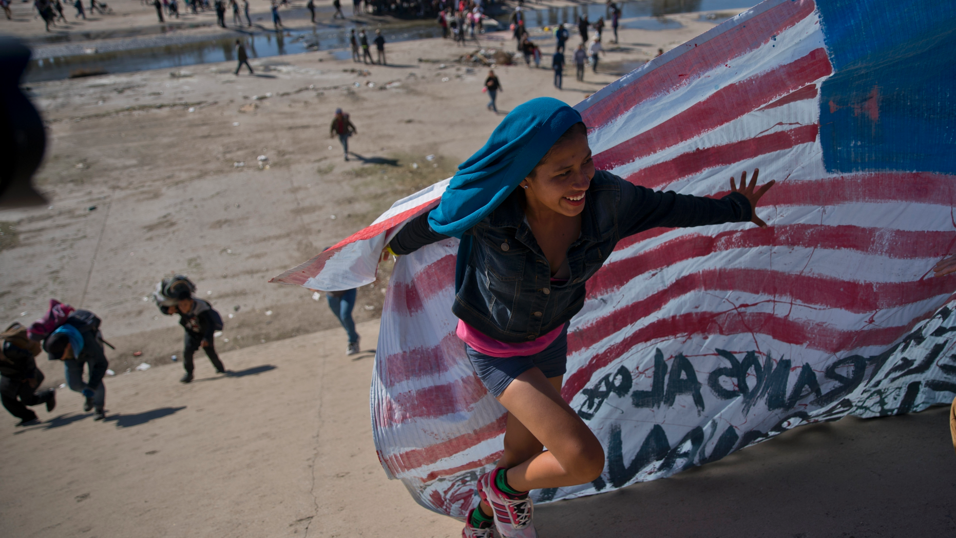 FILE - In this Nov. 25, 2018 file photo, a migrant woman helps carry a handmade U.S. flag up the riverbank at the Mexico-U.S. border. (AP Photo/Ramon Espinosa, File)