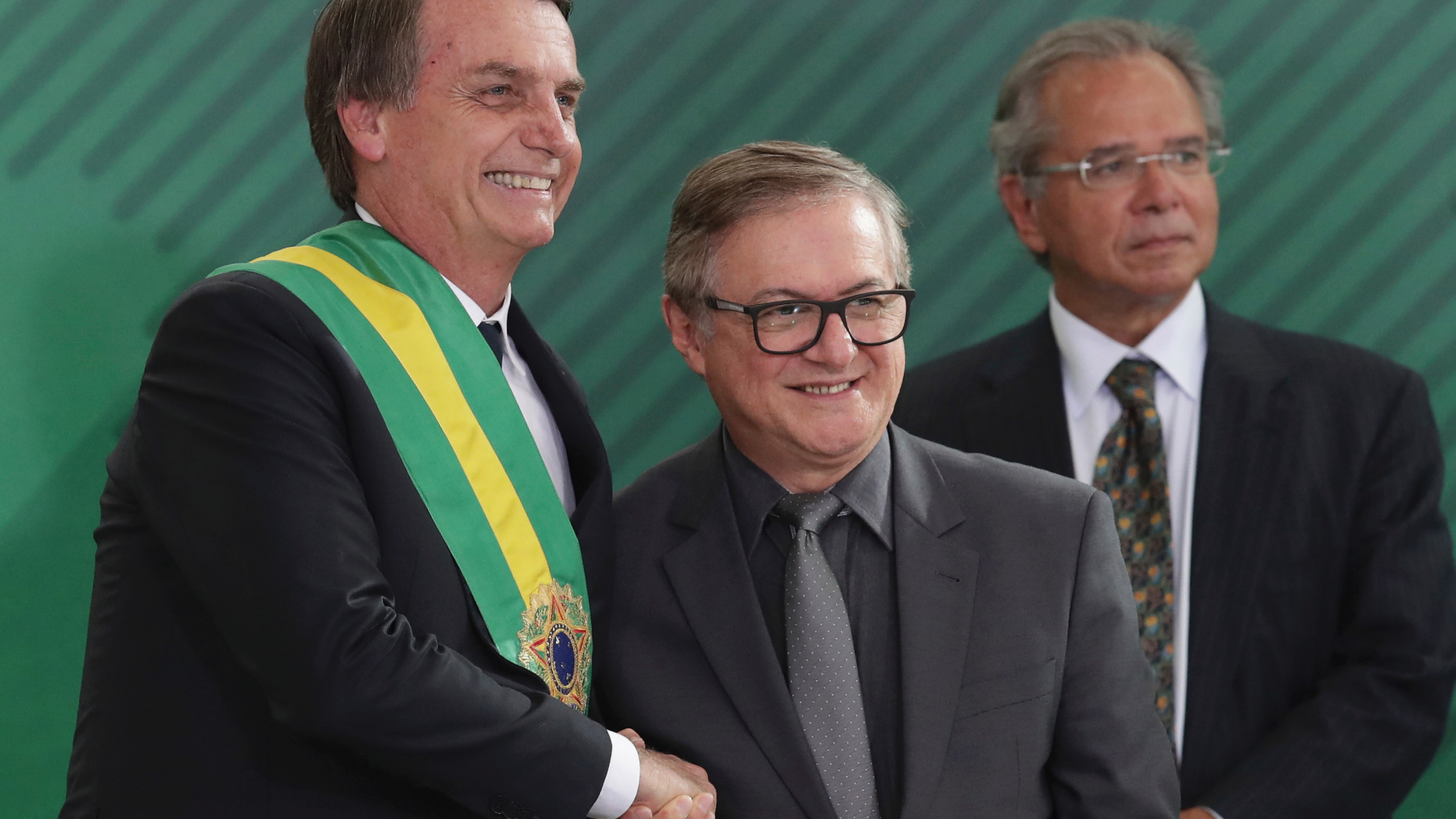 In this Jan. 1, 2019 photo, Brazil's President Jair Bolsonaro, left, shakes hands with Education Minister Ricardo Velez Rodriguez, during a swearing-in ceremony for his cabinet at the Planalto presidential palace, in Brasilia, Brazil. Velez Rodriguez said on Wednesday, April 3, 2019, that he will have school books revised to refer to the 1964 military coup as a “democratic regime by force.” (AP Photo/Eraldo Peres)