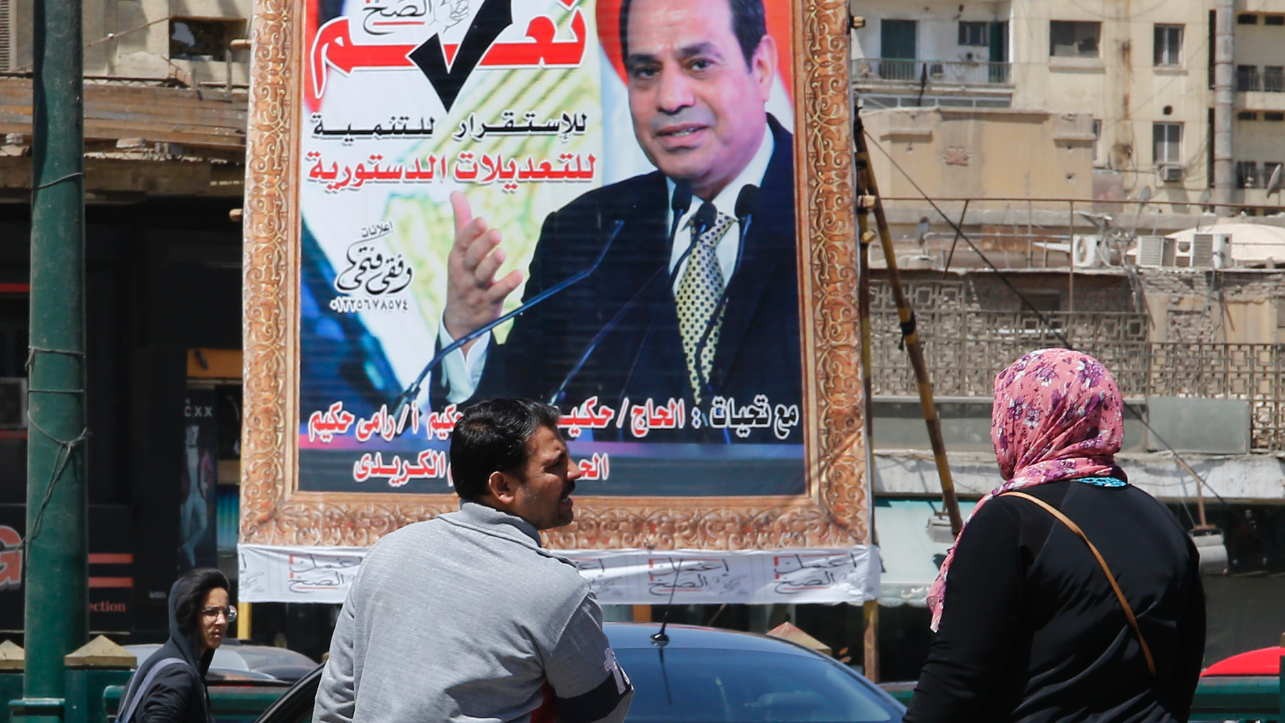 People walk past a banner supporting proposed amendments to the Egyptian constitution with a poster of Egyptian President Abdel-Fattah el-Sissi in Cairo, Egypt, Tuesday, April 16, 2019. Egypt's parliament was holding its last debate Tuesday on proposed amendments to the constitution that could see President Abdel-Fattah el-Sissi remain in power until 2030. Arabic reads, "do the right thing, yes to the developments, stability and amendments to the the constitution".(AP Photo/Amr Nabil)