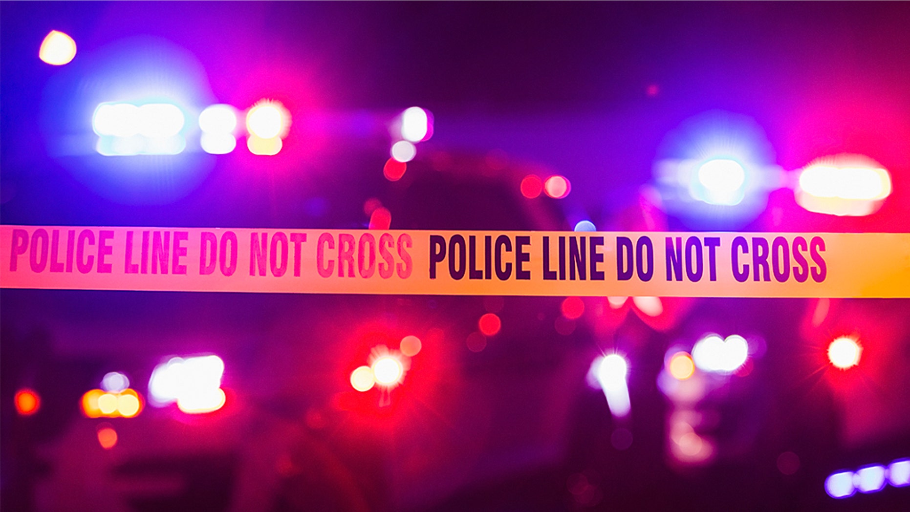 Accident or crime scene cordon tape, police line do not cross. It is nighttime, emergency lights of police cars flashing blue, red and white in the background