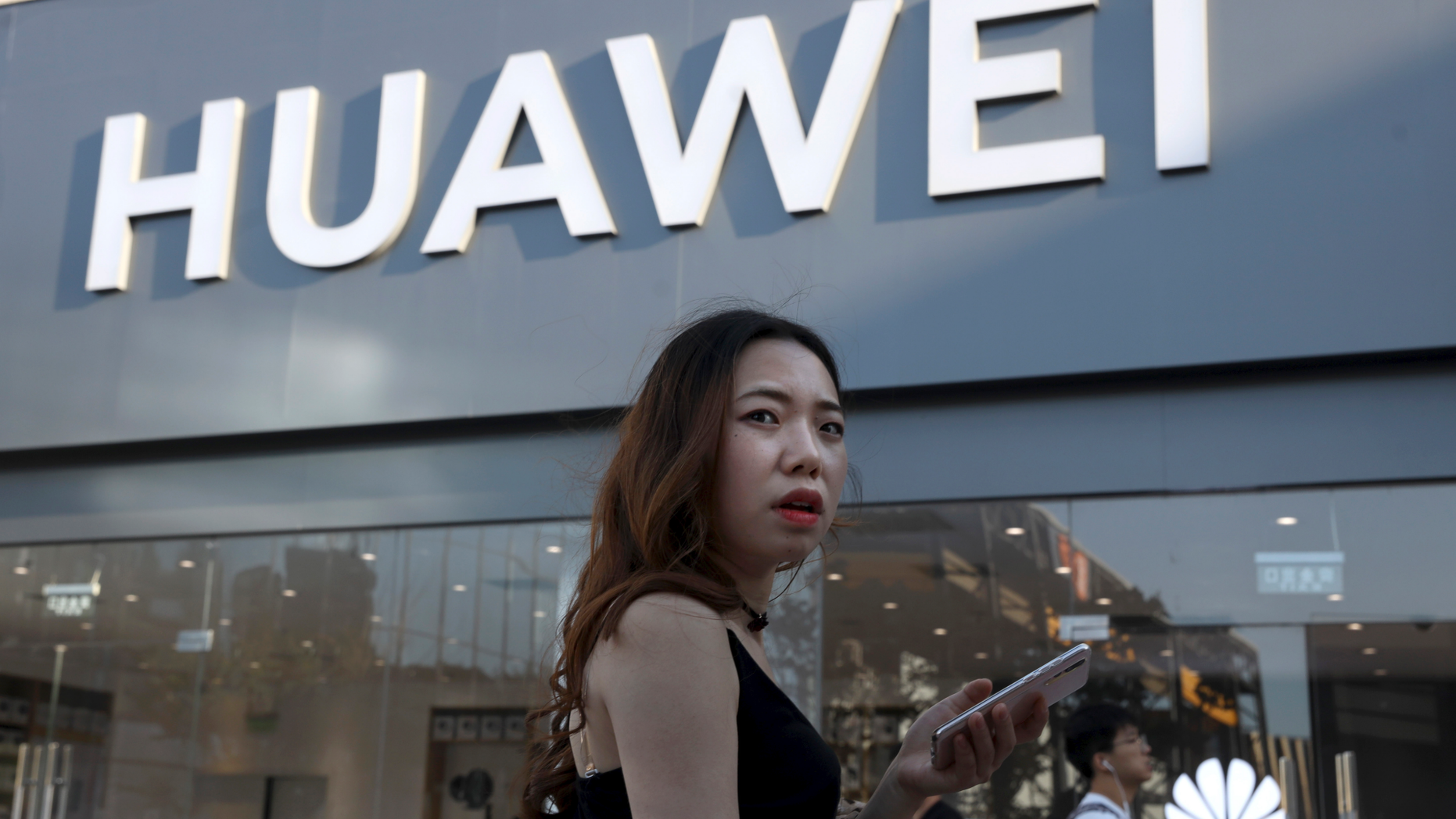 A woman uses a smartphone outside a Huawei store in Beijing Monday, May 20, 2019. Google is assuring users of Huawei smartphones the American company's services still will work on them following U.S. government restrictions on doing business with the Chinese tech giant. (AP Photo/Ng Han Guan)
