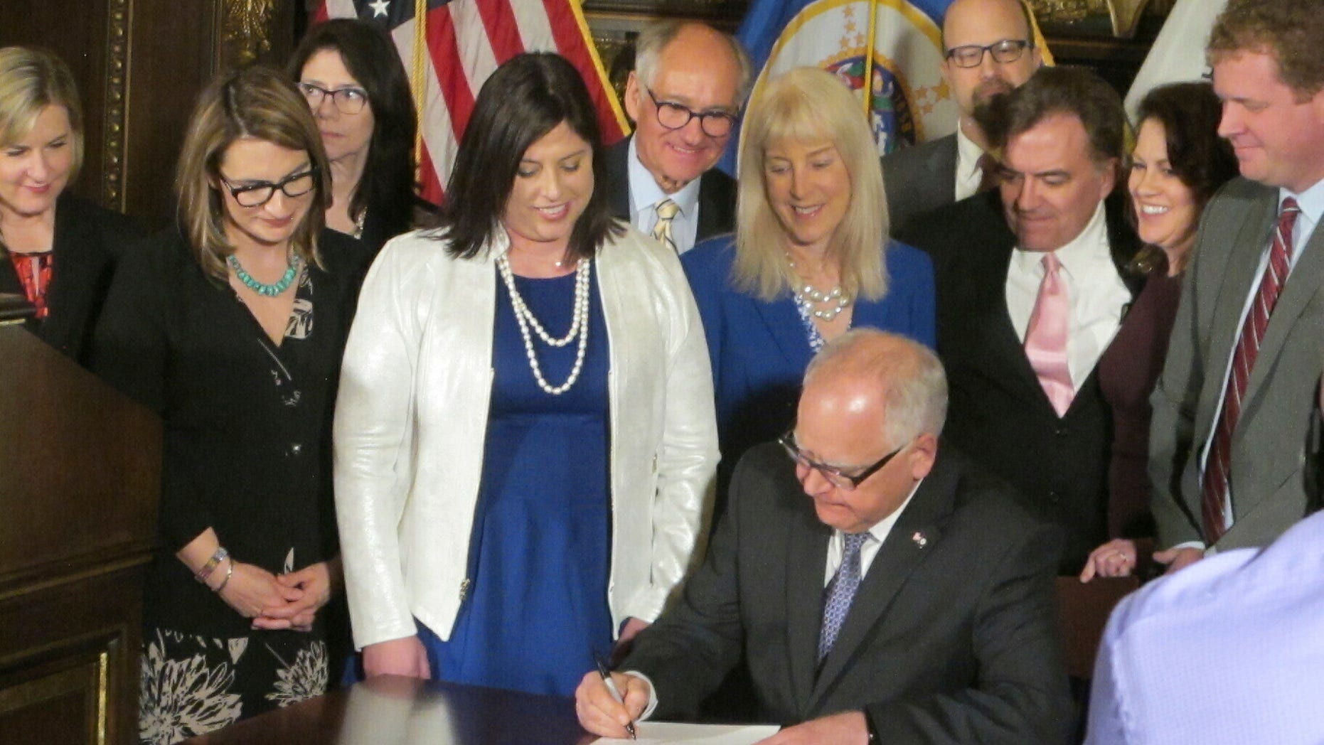 Jenny Teeson, center in white, of Andover, Minnesota, looks on as Minnesota Gov. Tim Walz signs a bill at the Capitol in St. Paul, on Thursday, May 2, 2019, repealing a Minnesota law that prevented prosecutors from filing sexual assault charges against people accused of raping their spouse. Teeson, testified before legislative committees earlier this year about how her now ex-husband drugged her and made a video of himself raping her while she was unconscious. Prosecutors dropped rape charges because of the old law, and he served just 30 days in jail for invasion of privacy. (AP Photo/Steve Karnowski)