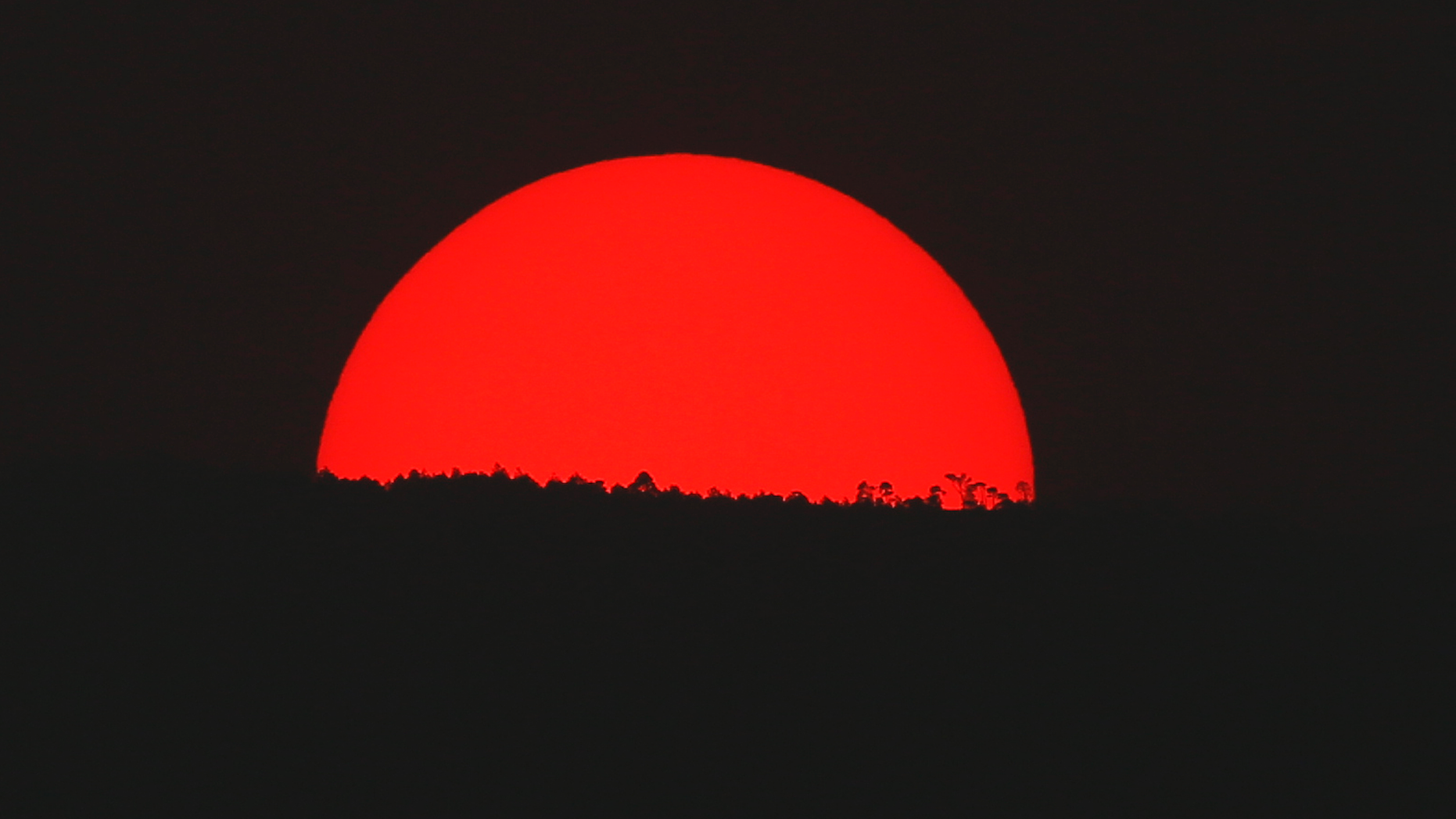 Tinted blood red by a thick cloud of smoke and pollution, the sun sets on the mountains above Mexico City, Monday, May 13, 2019. Mexico City's government has warned residents to remain indoors as forest and brush fires carpeted the metropolis in a smoky haze that has alarmed even many of those accustomed to living with air pollution. (AP Photo/Marco Ugarte)