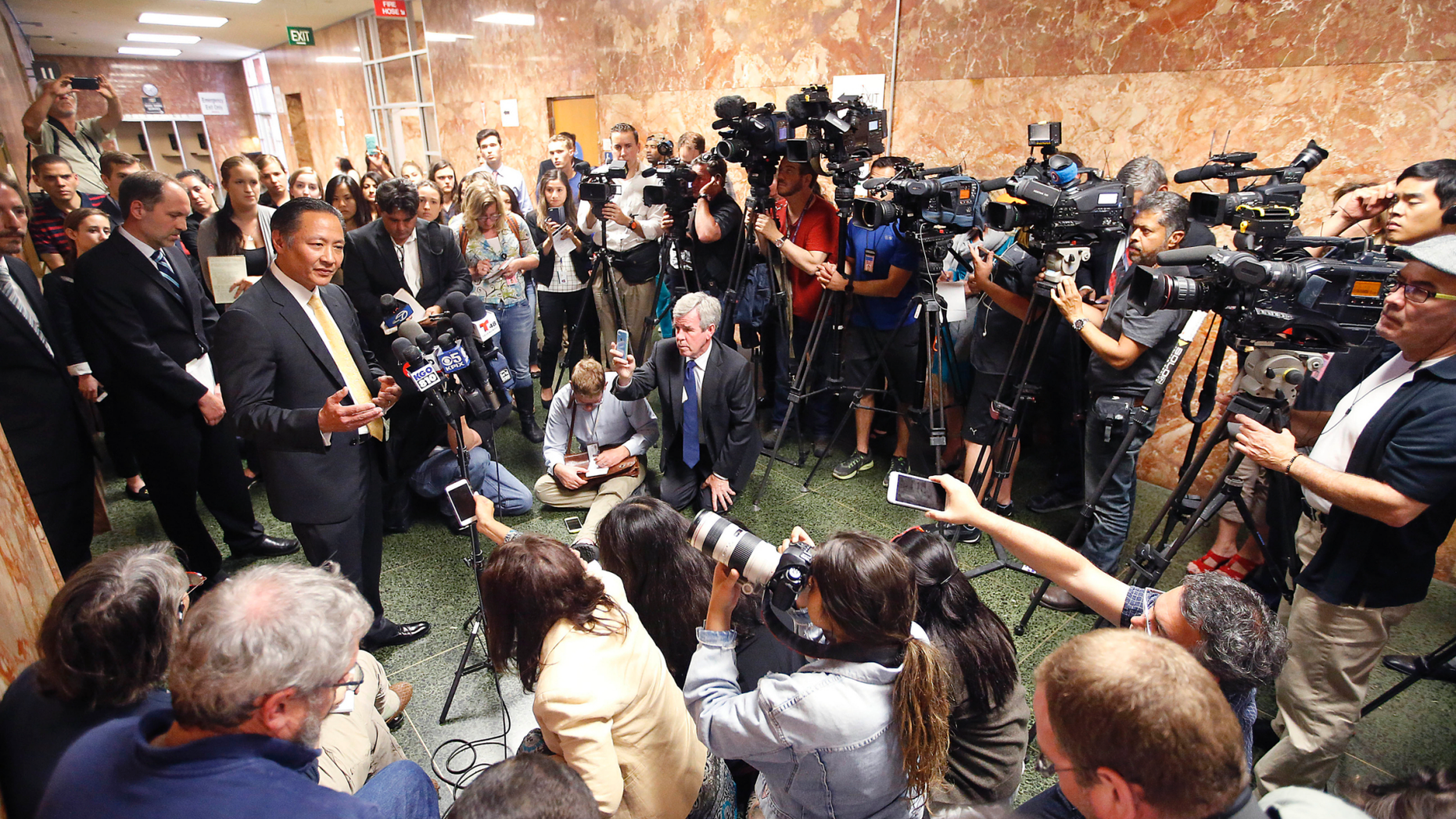 FILE - In this July 7, 2015, file photo, San Francisco Public Defender Jeff Adachi, left, talks to members of the media after Francisco Sanchez' arraignment in San Francisco. A freelance journalist is vowing to protect his source after San Francisco police raided his home and office as part of a criminal investigation. Bryan Carmody tells the Los Angeles Times that officers handcuffed him Friday, May 10, 2019, as they confiscated items including his cell phone, computer and cameras. Authorities say the raid came during an ongoing probe into who leaked a confidential police report about the Feb. 22 death Adachi. (AP Photo/Tony Avelar, File)