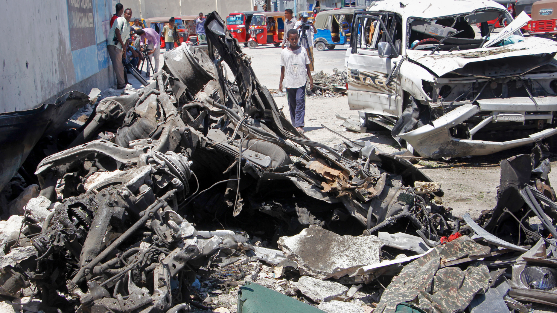Somalis walk near the wreckage after a suicide car bomb attack in the capital Mogadishu, Somalia Wednesday, May 22, 2019. A police spokesman said the attack killed at least six people and injured more than a dozen, while Islamic extremist group al-Shabab claimed responsibility for the blast, saying it targeted vehicles carrying government officials. (AP Photo/Farah Abdi Warsameh)