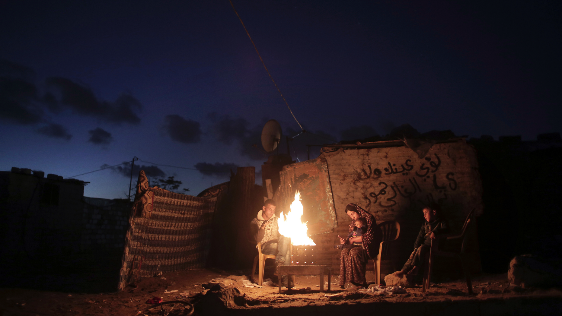 File - In this Jan. 15, 2017 file photo, a Palestinian family warm up outside their makeshift house during a power cut in Khan Younis in the southern Gaza Strip. Qatar's Foreign Ministry said Tuesday, May 7, 2019, that it will send $480 million to Palestinians in the West Bank and the Gaza Strip after a cease-fire deal ended the deadliest fighting between Israel and Palestinian factions since a 2014 war. A statement from Qatar said $300 million would support health and education programs of the Palestinian Authority, while $180 million would go toward "urgent humanitarian relief" in United Nations programs and toward electricity. (AP Photo/ Khalil Hamra, File)