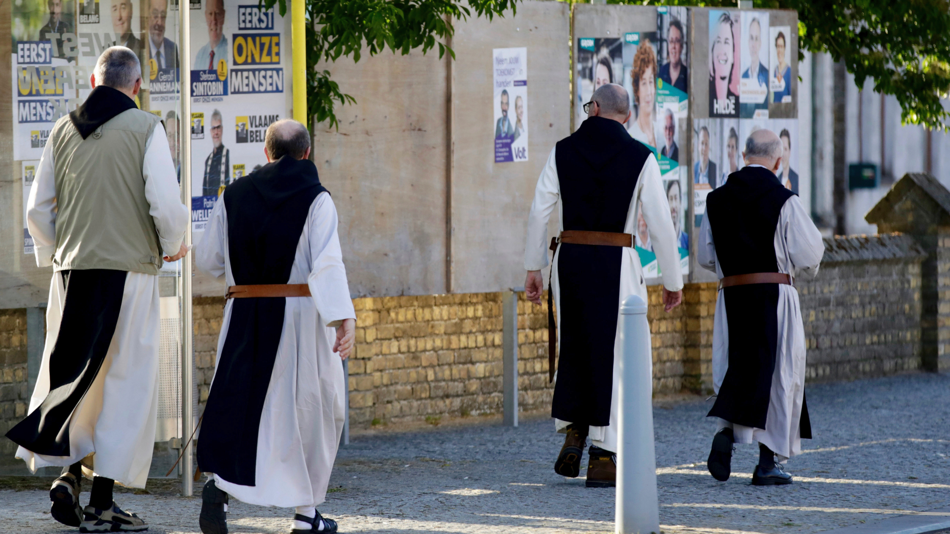 Monks from the Saint Sixtus Trappist Abbey walk by election campaign posters as they walk to a polling station in Westvleteren, Belgium, Sunday, May 26, 2019. Belgium, which has one of the oldest compulsory voting systems, goes to the polls Sunday to vote on the regional, federal and European level. (AP Photo/Olivier Matthys)