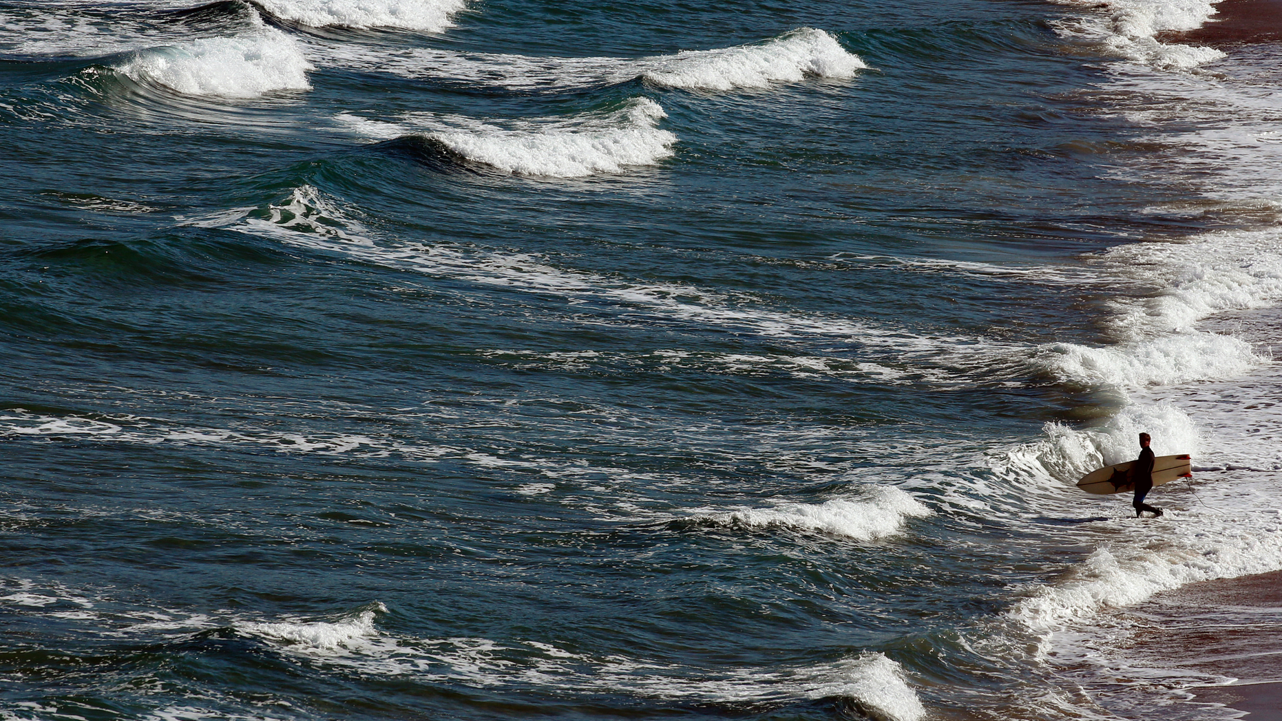 A surfer goes to the Atlantic sea in Biarritz, southwestern France, Tuesday May 14, 2019. Temperatures in southwestern France reached 20 degrees Celsius (68 Fahrenheit). (AP Photo/Bob Edme)