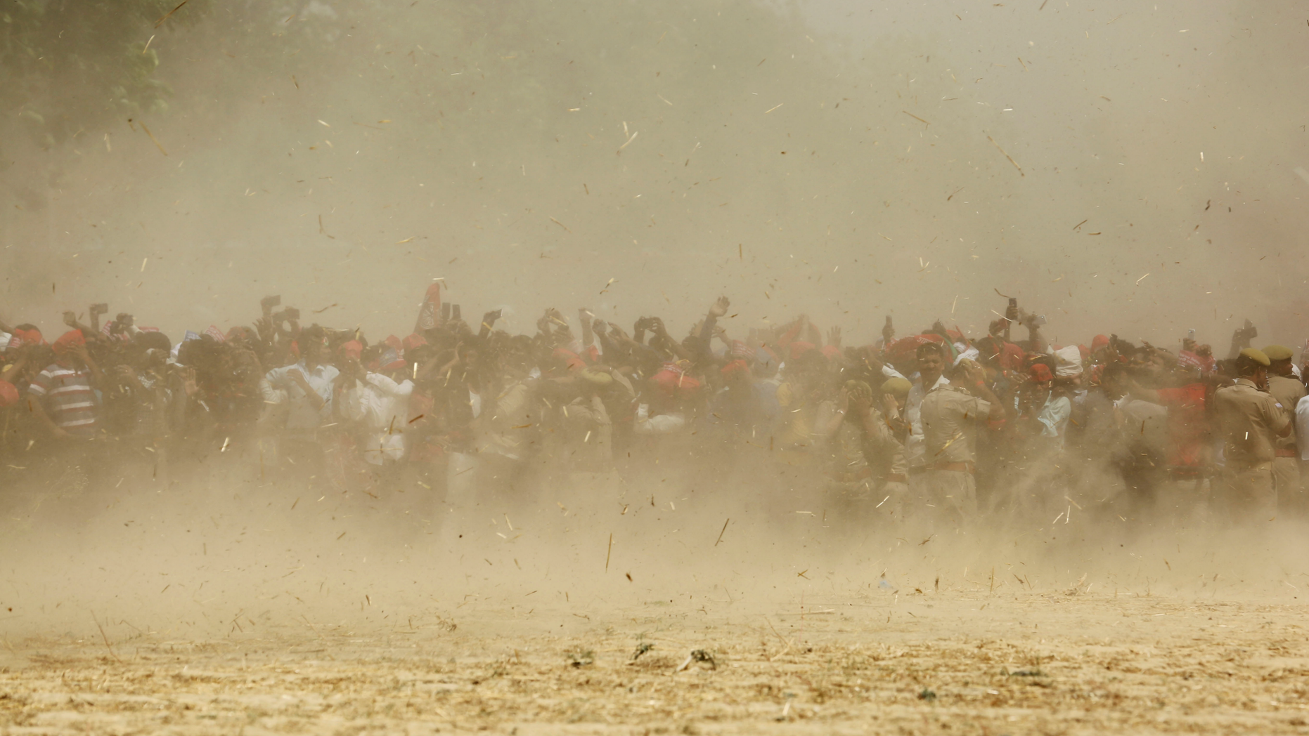 Supporters of Samajwadi Party president Akhilesh Yadav are seen through dust as a helicopter carrying Yadav lands at an election rally venue in Prayagraj, Uttar Pradesh, India, Sunday, May 5, 2019. With 900 million of India's 1.3 billion people registered to vote, the Indian national election is the world's largest democratic exercise. (AP Photo/Rajesh Kumar Singh)