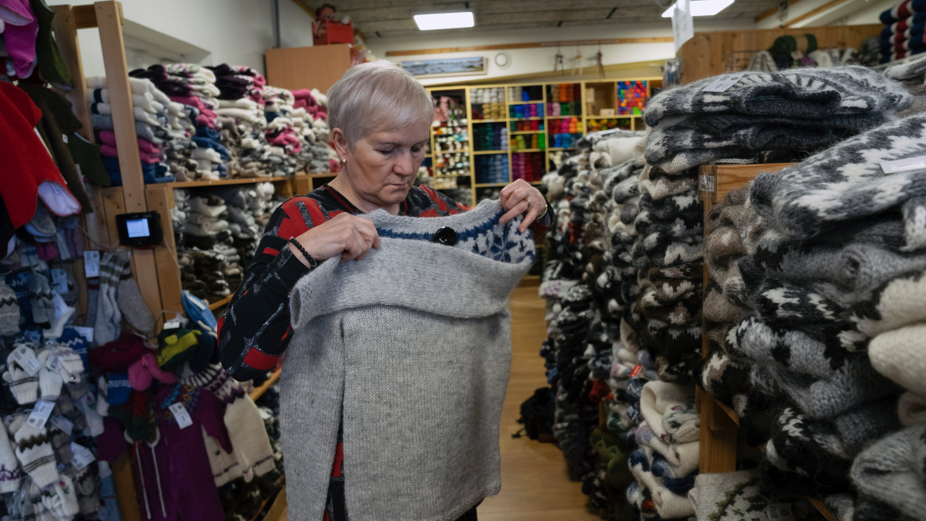 In this photo taken on Tuesday, April 30, 2019, Thuridur Einarsdottir, founder of the Handknitting Association of Iceland, folds a 'lopi' sweater in Reykjavik. Trouble is rattling one of Iceland’s most distinctive industries: the production of the thick, hand-knitted “lopi” sweaters adored by tourists and worn with pride by locals. The individually produced, very warm sweaters have become a symbol of Iceland. But increasingly the local wool is being shipped to the cheaper labor market of China, where the sweaters are hand-knitted and then sent back for sale on the North Atlantic island. (AP Photo/Egill Bjarnason)